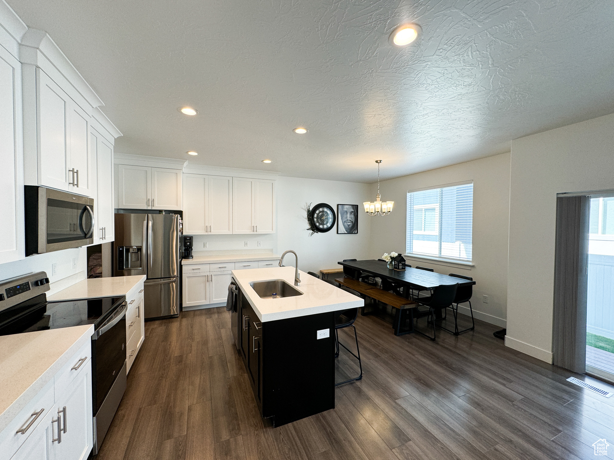 Kitchen with white cabinetry, stainless steel appliances, decorative light fixtures, a kitchen island with sink, and sink