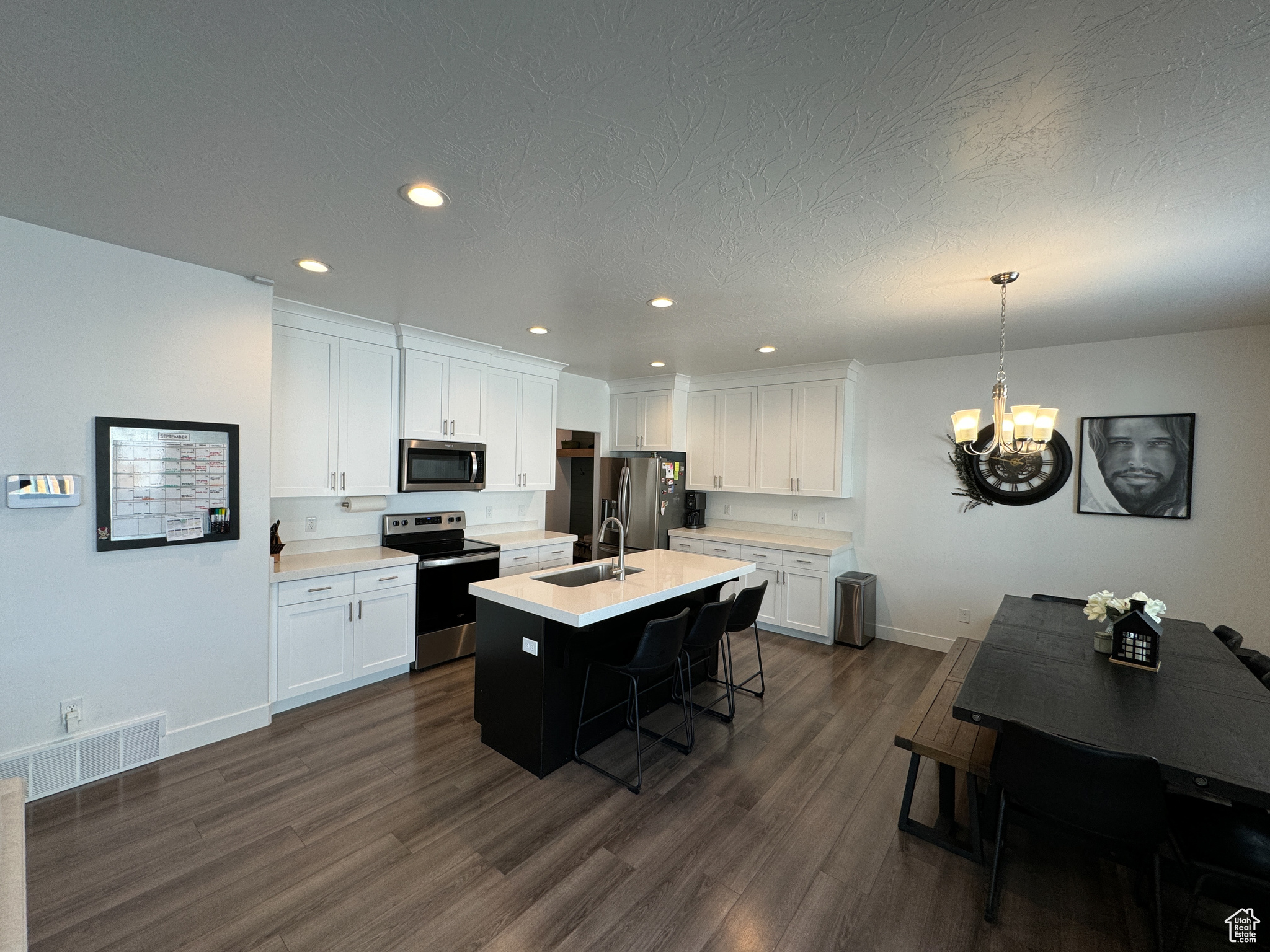 Kitchen featuring a kitchen island with sink, white cabinets, appliances with stainless steel finishes, and decorative light fixtures