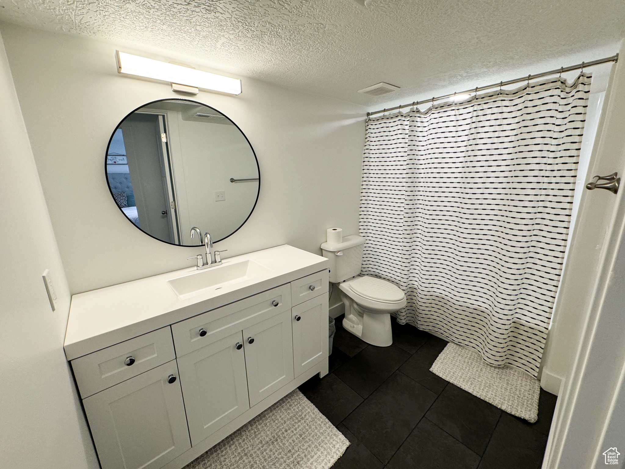 Bathroom with tile patterned flooring, a textured ceiling, vanity, and toilet