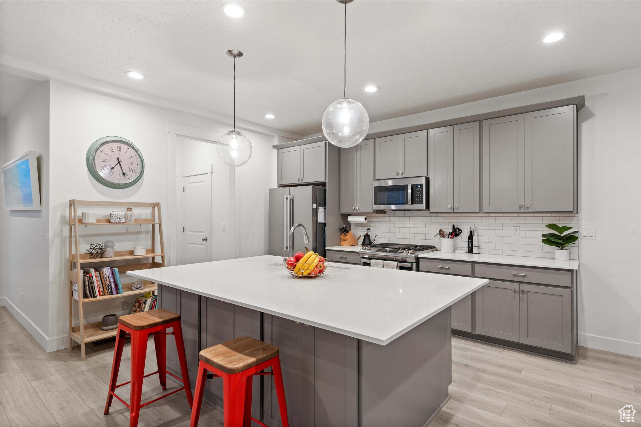 Kitchen with pendant lighting, gray cabinets, stainless steel appliances, light wood-type flooring, and a kitchen bar