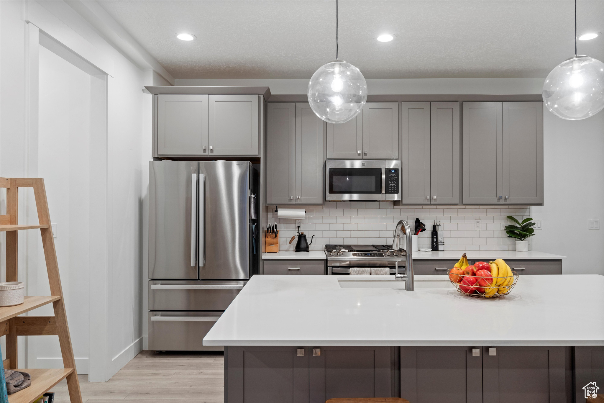 Kitchen with appliances with stainless steel finishes, backsplash, light hardwood / wood-style floors, and gray cabinets