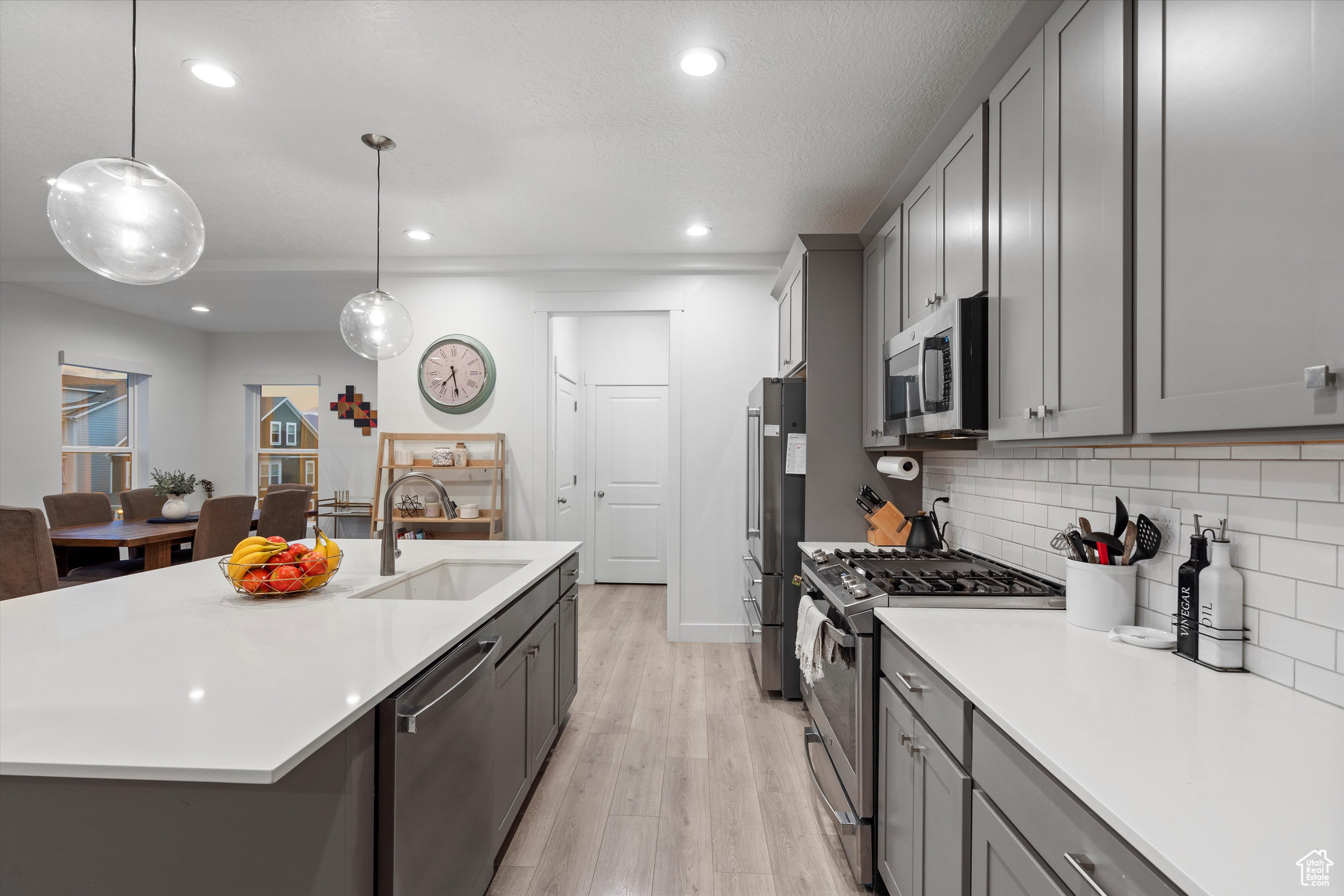 Kitchen facing toward entrance to pantries and 1/2 bath, center island with sink, decorative light fixtures, stainless steel appliances, and light hardwood / wood-style floors