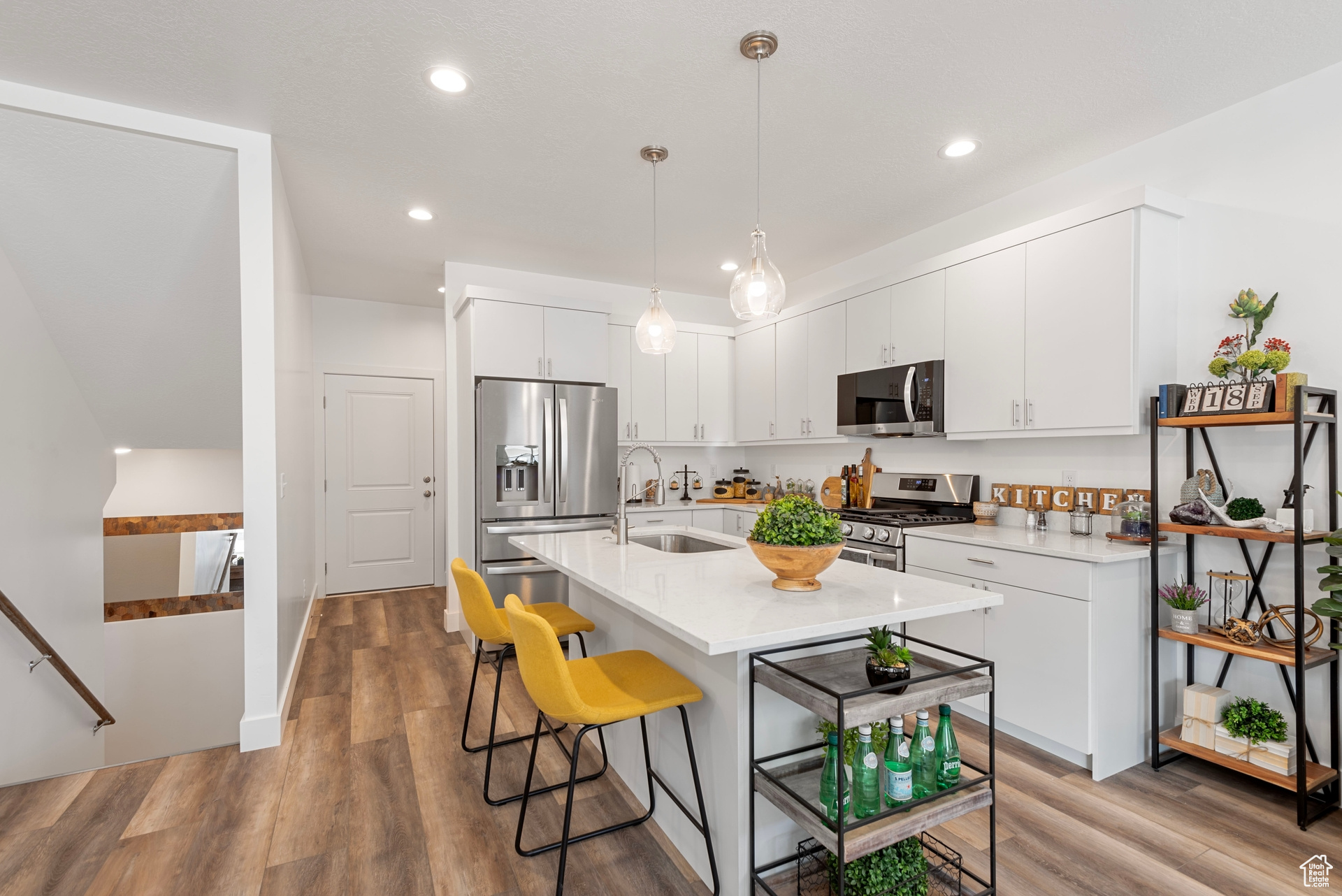 Kitchen with white cabinetry, pendant lighting, stainless steel appliances, light hardwood / wood-style flooring, and sink