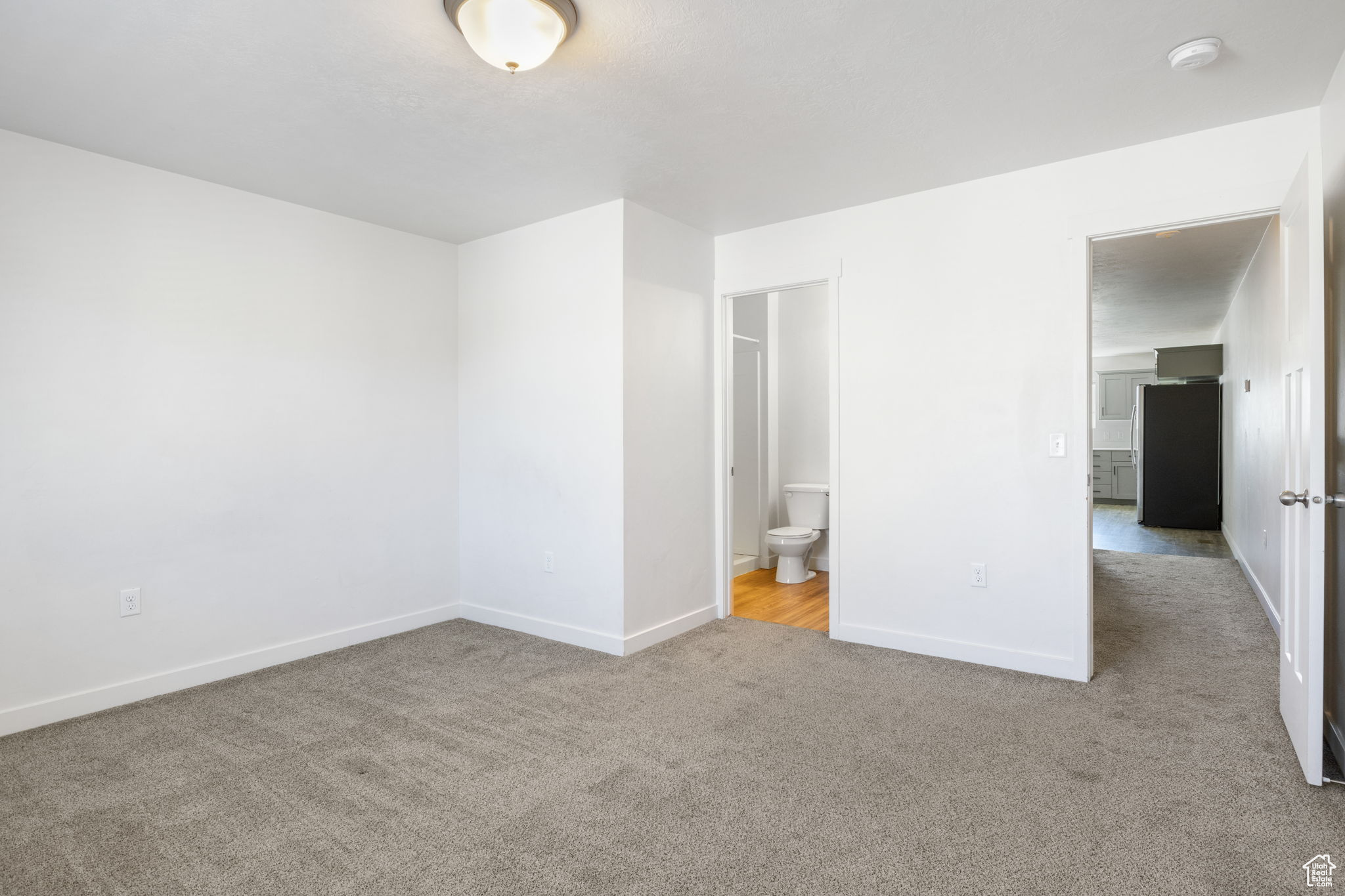 Unfurnished bedroom with light carpet, stainless steel fridge, and ensuite bathroom