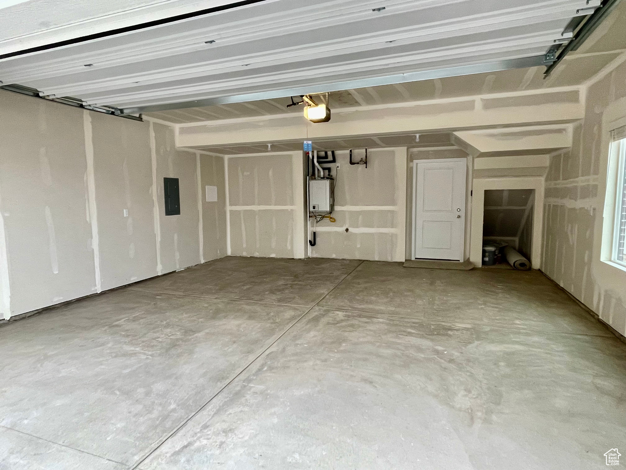 Garage featuring a garage door opener, electric panel, and tankless water heater