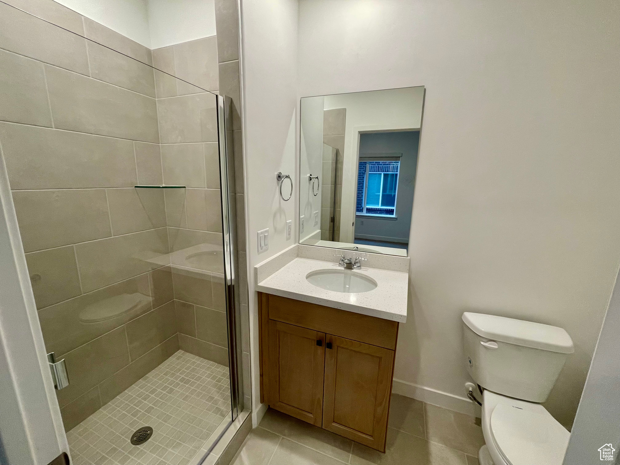 Bathroom with toilet, an enclosed shower, and tile patterned flooring