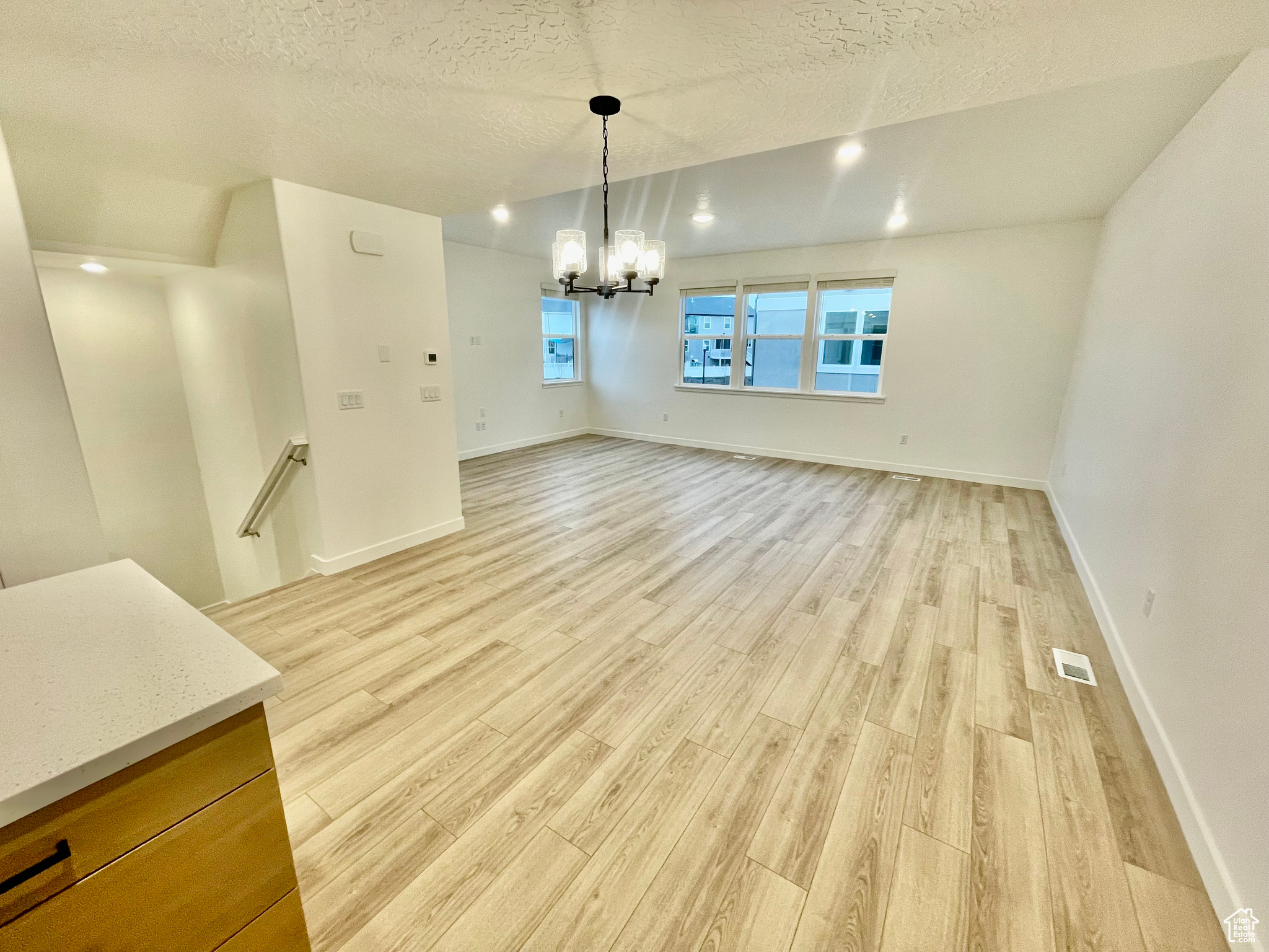 Unfurnished dining area featuring light wood-type flooring, a textured ceiling, and a notable chandelier