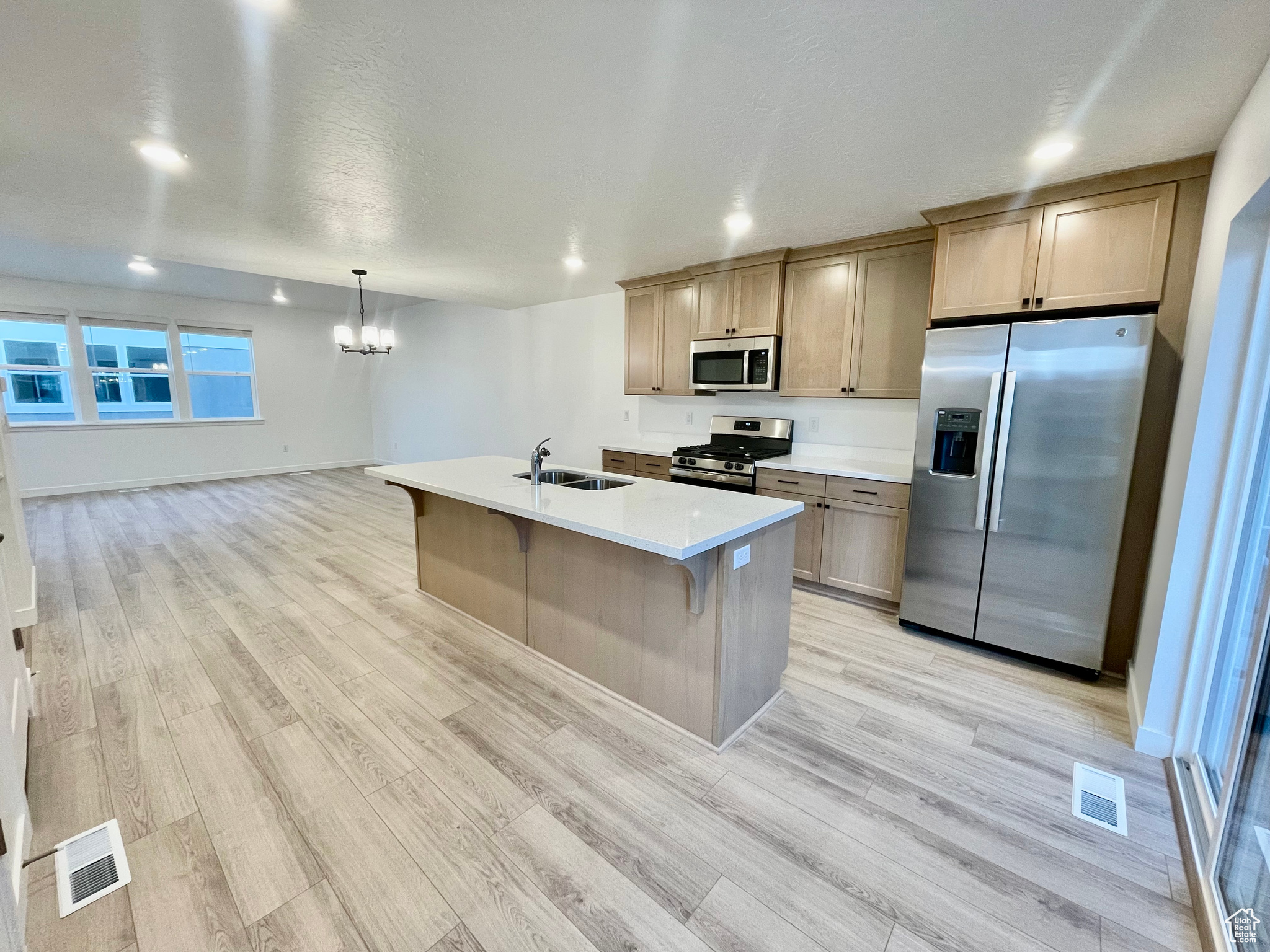 Kitchen with sink, decorative light fixtures, a center island with sink, light wood-type flooring, and appliances with stainless steel finishes