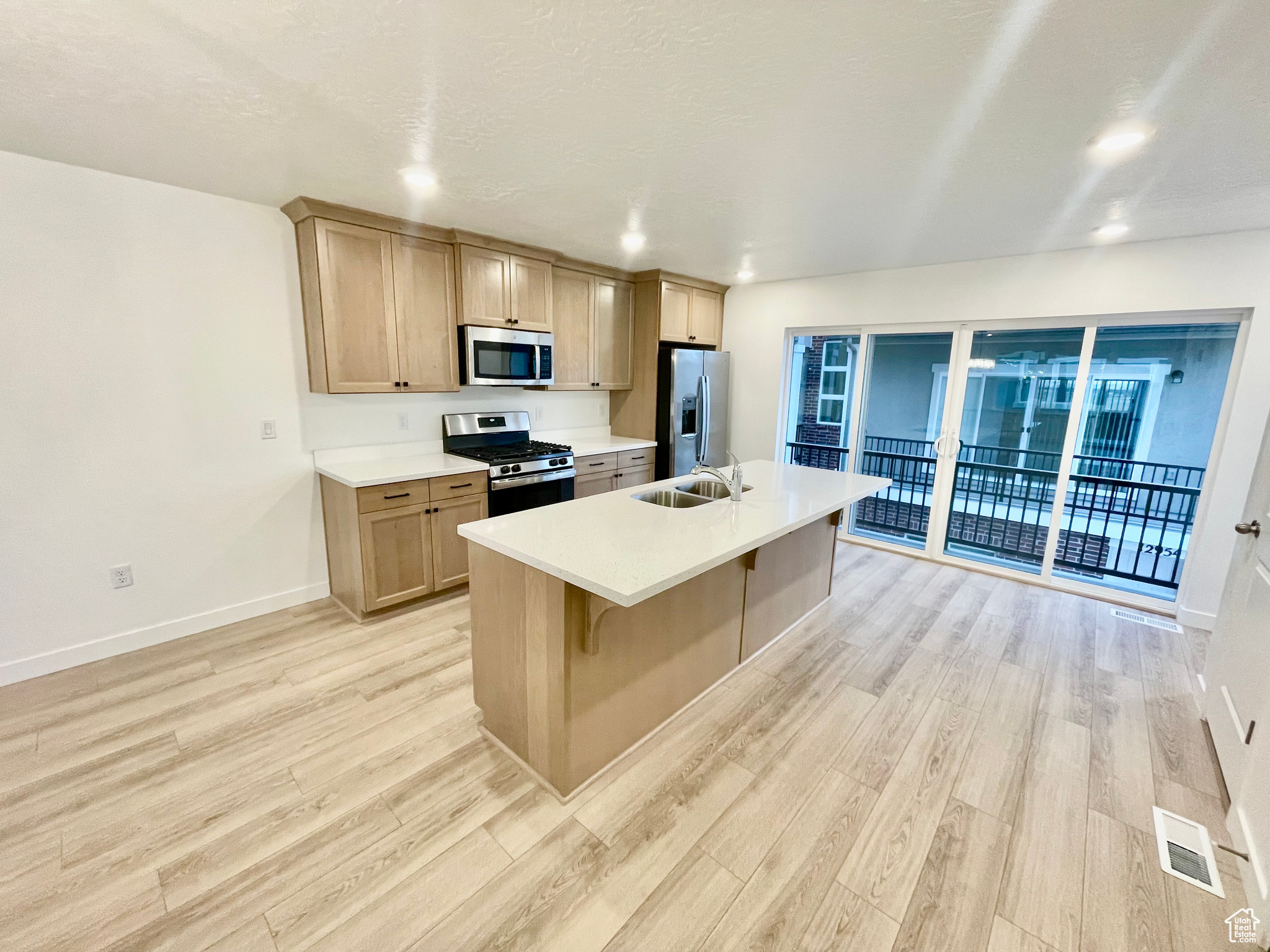 Kitchen featuring sink, a kitchen island with sink, a kitchen breakfast bar, stainless steel appliances, and light brown cabinetry