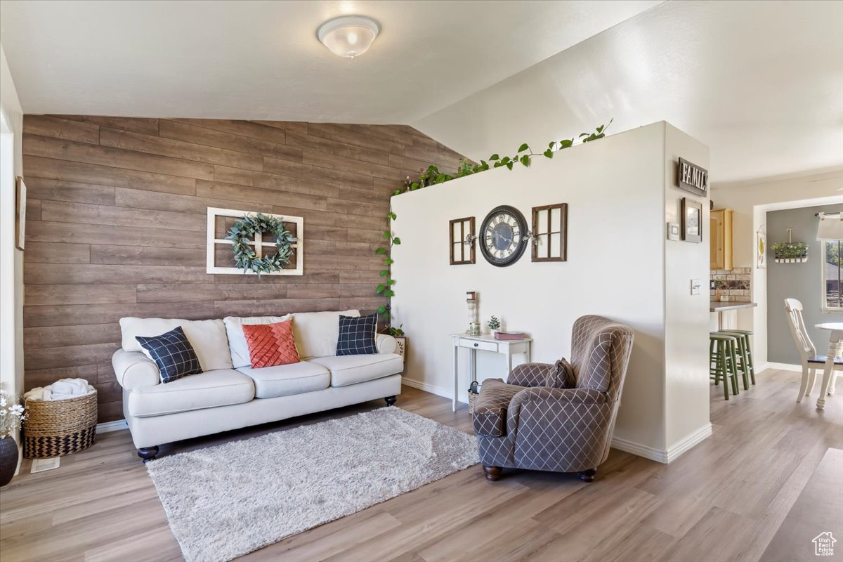 Living room featuring light hardwood / wood-style floors, lofted ceiling, and wood walls