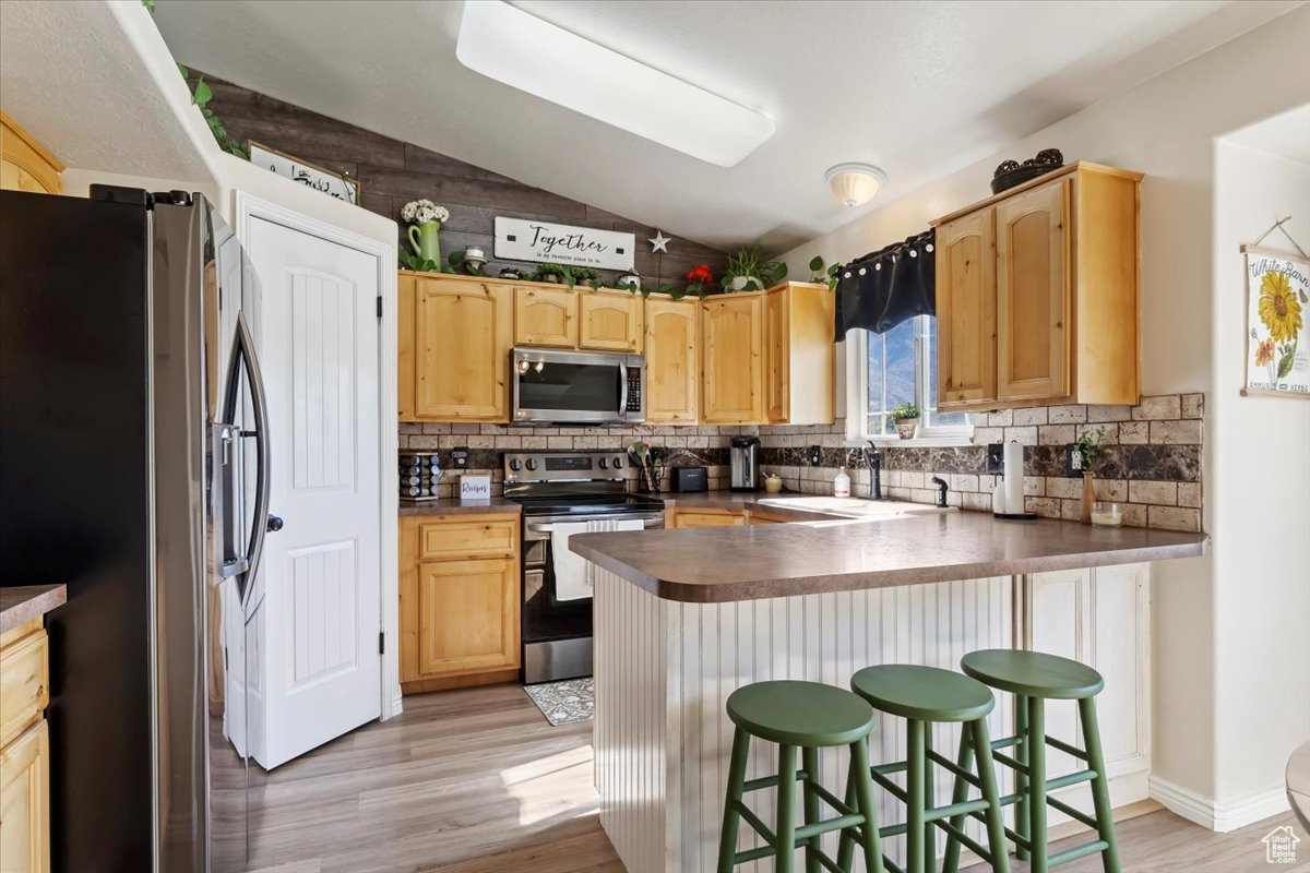 Kitchen featuring vaulted ceiling, kitchen peninsula, a breakfast bar area, stainless steel appliances, and sink