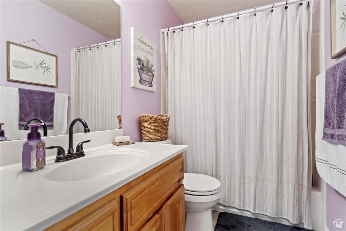 Full bathroom with vanity, toilet, a textured ceiling, and shower / bath combo