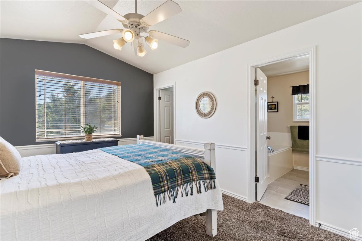 Bedroom with light colored carpet, lofted ceiling, ceiling fan, and ensuite bathroom