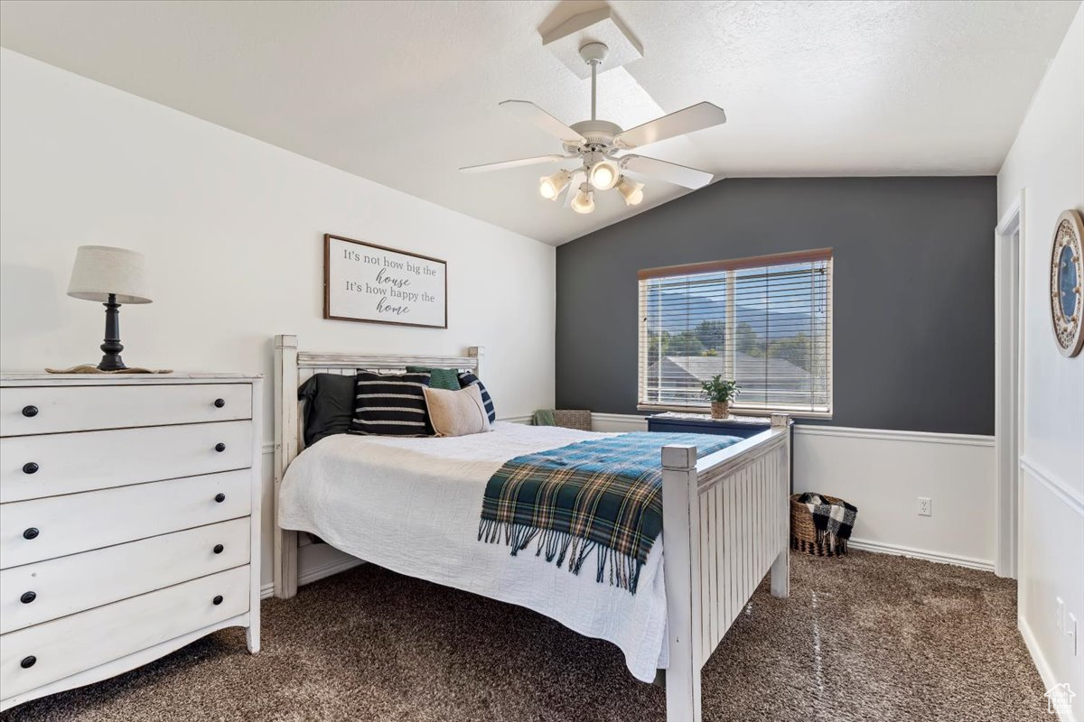 Carpeted bedroom featuring ceiling fan and vaulted ceiling