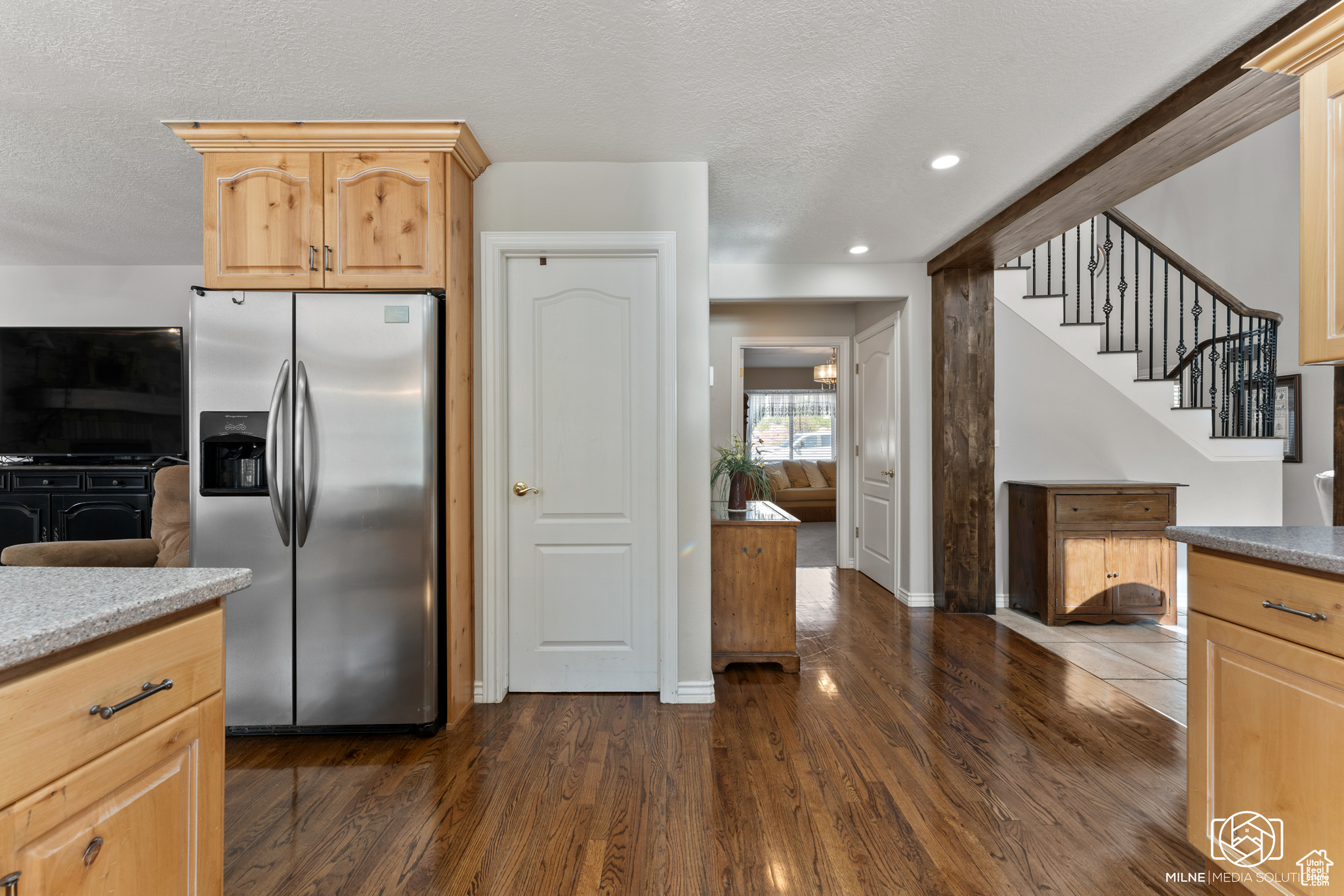 Kitchen featuring stainless steel refrigerator with ice dispenser, a textured ceiling, light brown cabinets, and dark wood-type flooring