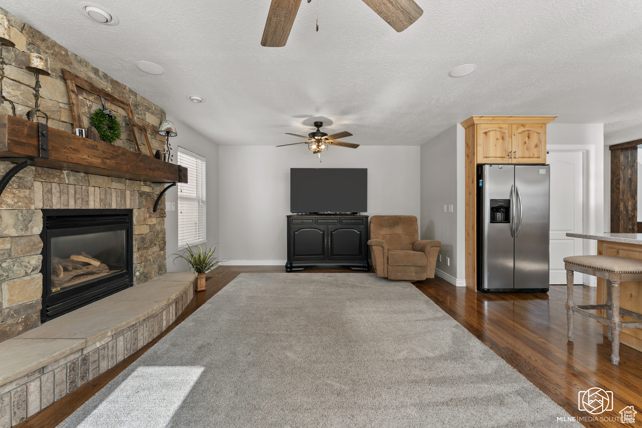 Living room featuring a textured ceiling, a fireplace, dark hardwood / wood-style floors, and ceiling fan