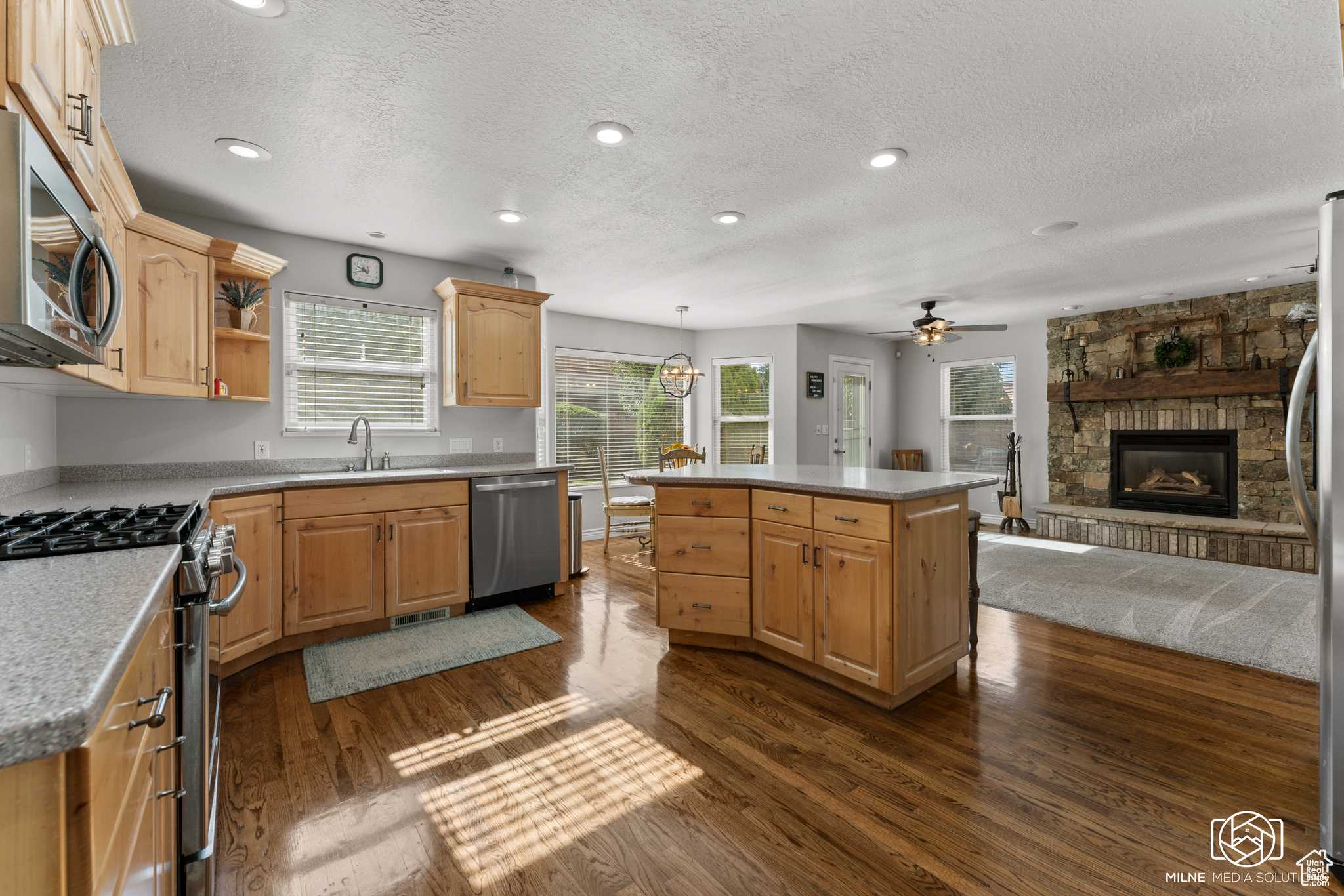 Kitchen featuring ceiling fan, a kitchen island, appliances with stainless steel finishes, a fireplace, and dark hardwood / wood-style flooring