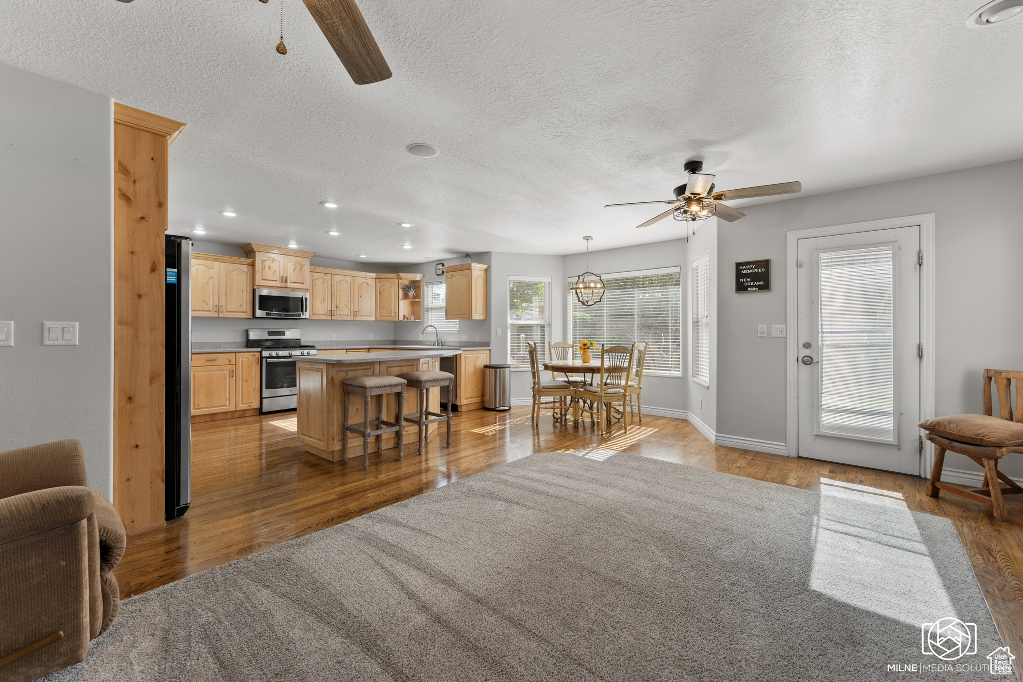 Interior space with ceiling fan, a kitchen island, hardwood / wood-style flooring, appliances with stainless steel finishes, and a breakfast bar