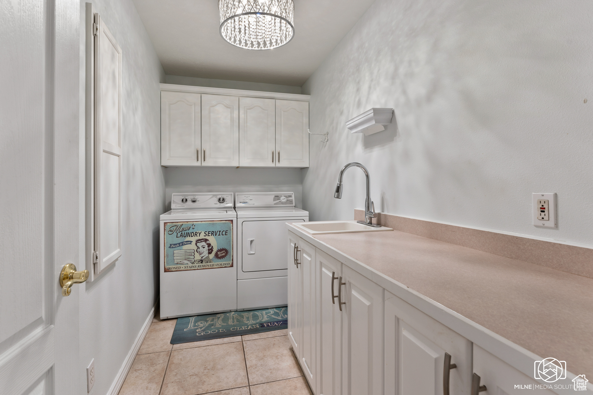 Clothes washing area featuring light tile patterned floors, sink, a chandelier, cabinets, and washer and dryer