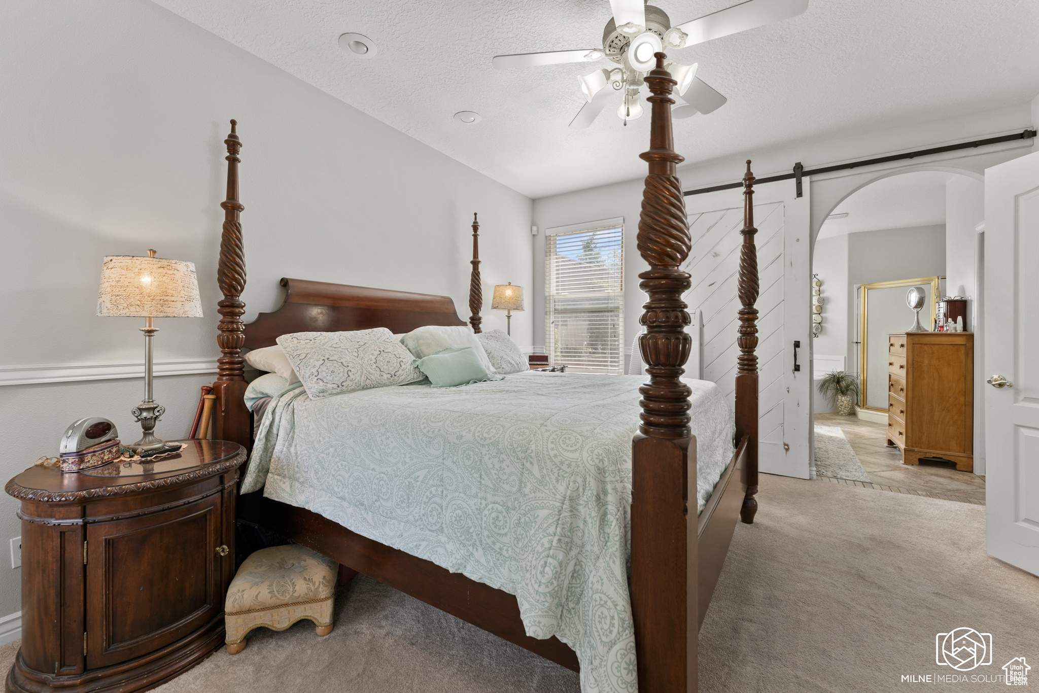 Bedroom with ceiling fan, a textured ceiling, light colored carpet, ensuite bath, and a barn door