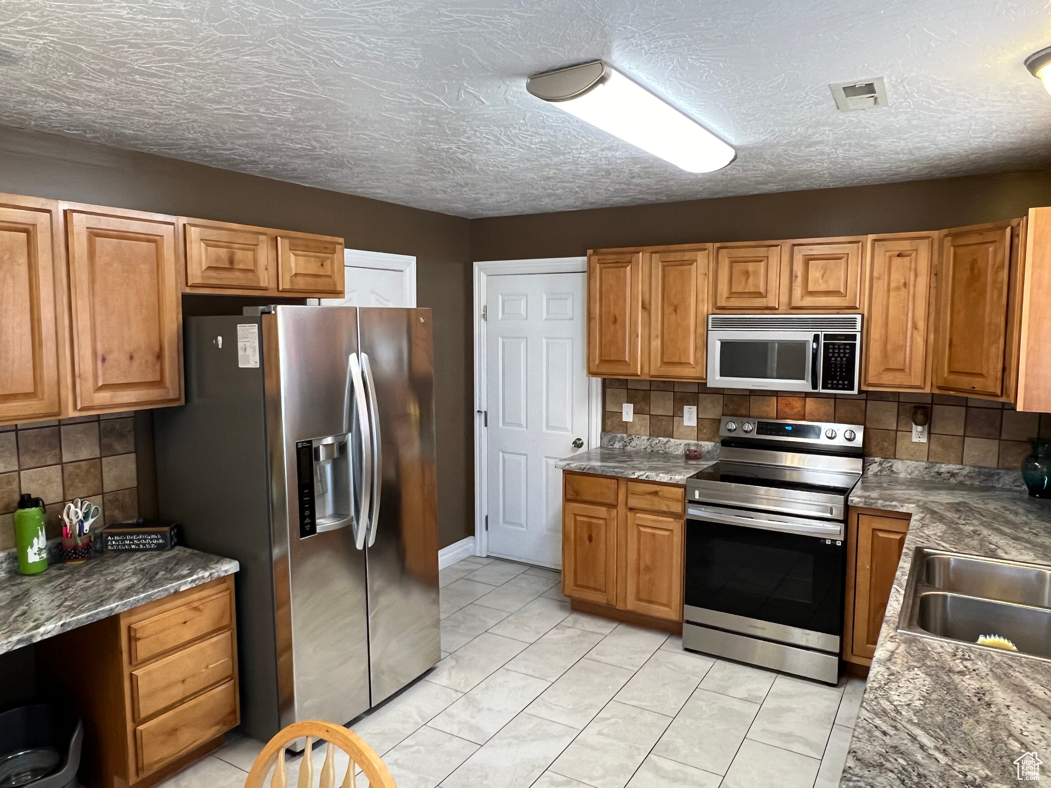 Kitchen with sink, light tile patterned floors, tasteful backsplash, stainless steel appliances, and dark stone countertops