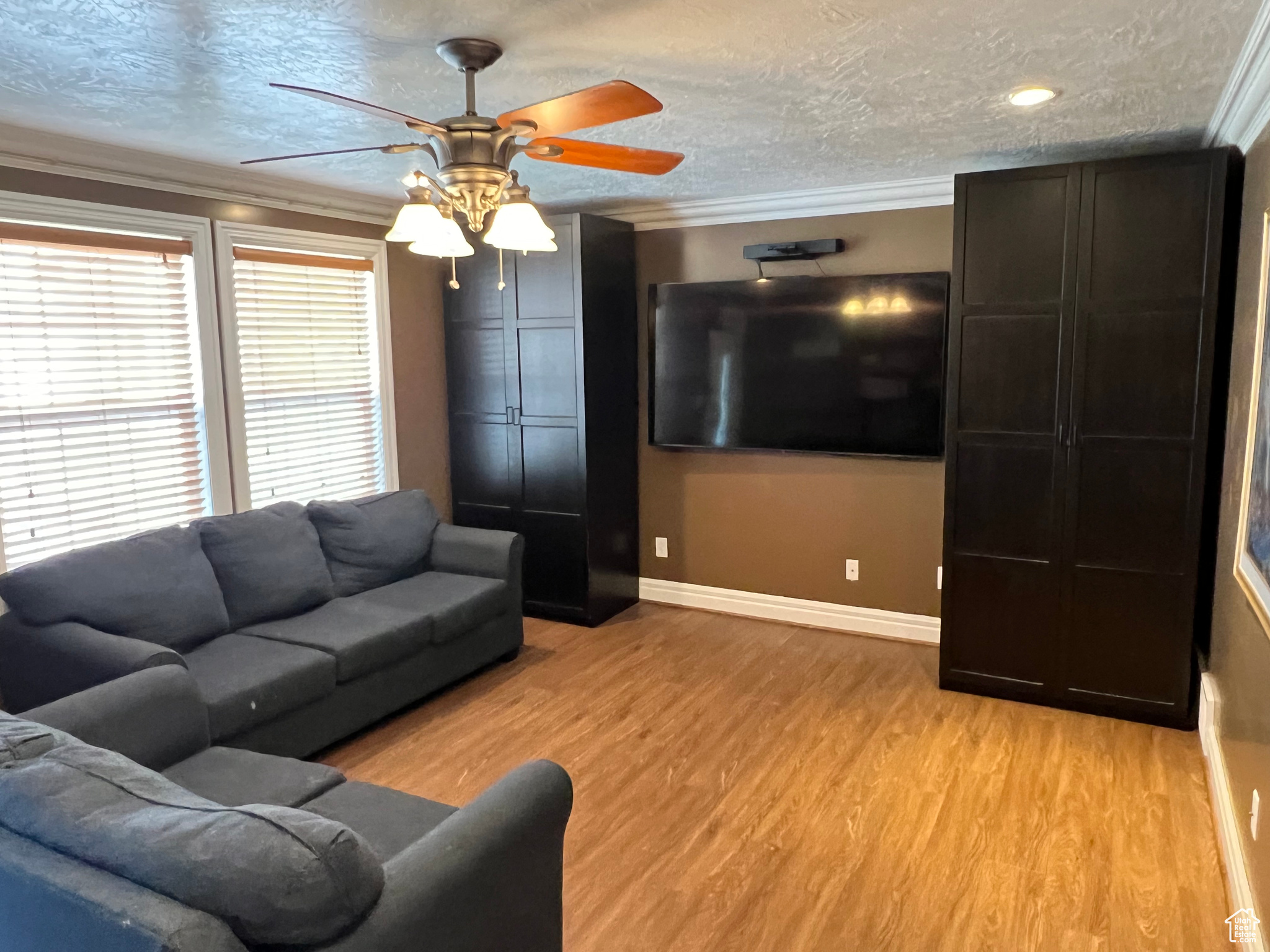 Living room featuring ceiling fan, a textured ceiling, light hardwood / wood-style floors, and ornamental molding