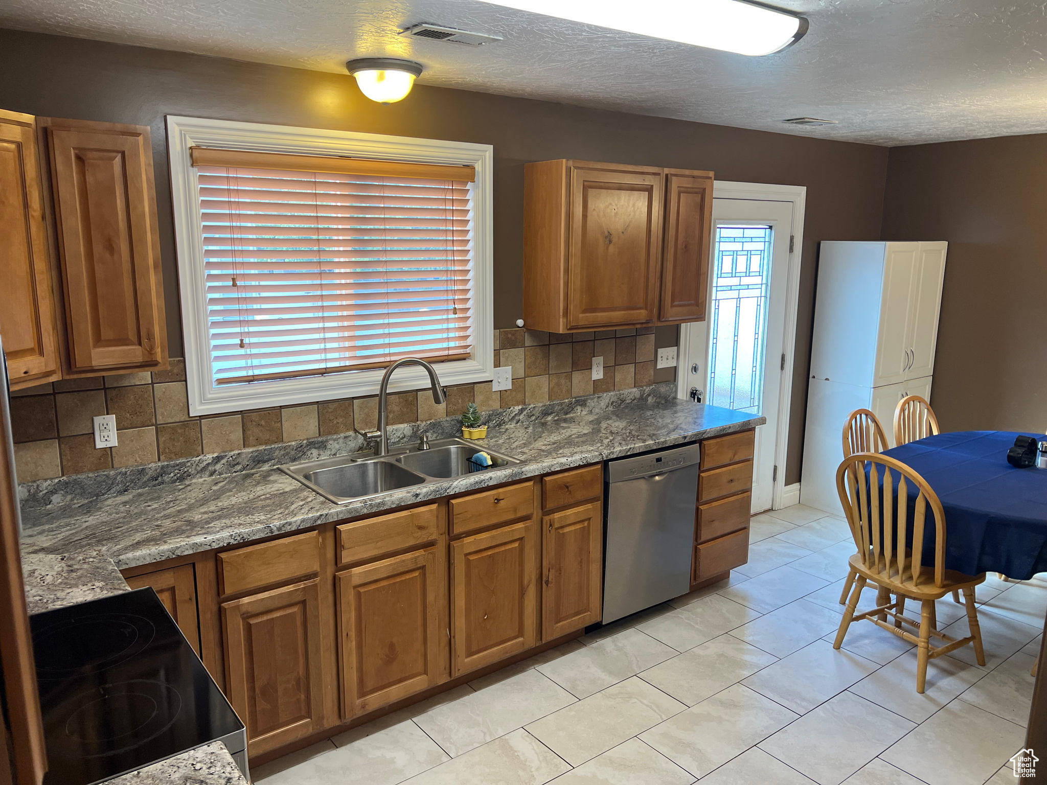 Kitchen with backsplash, sink, light tile patterned floors, and stainless steel dishwasher