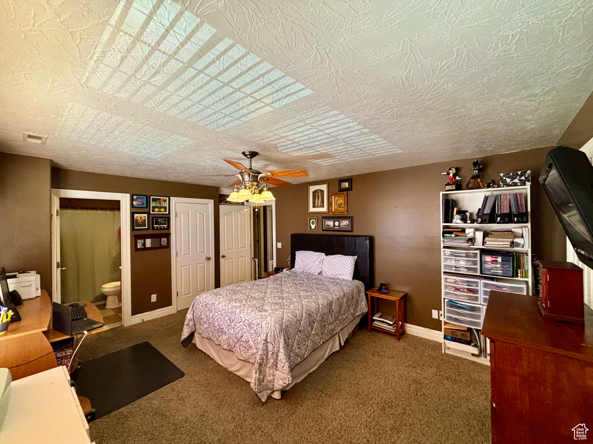 Bedroom with ceiling fan, a textured ceiling, ensuite bath, and dark colored carpet