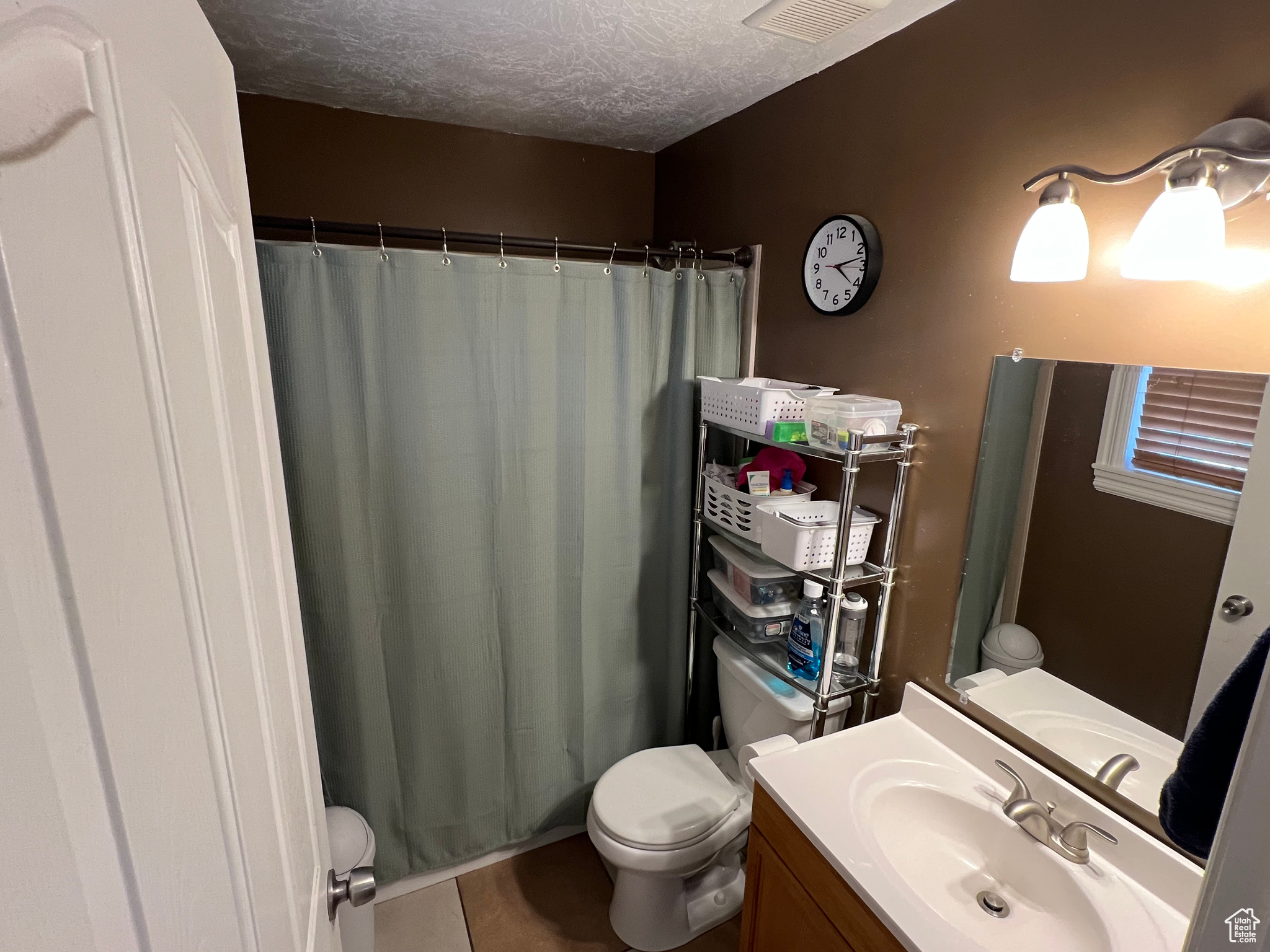 Bathroom with a textured ceiling, vanity, toilet, and walk in shower