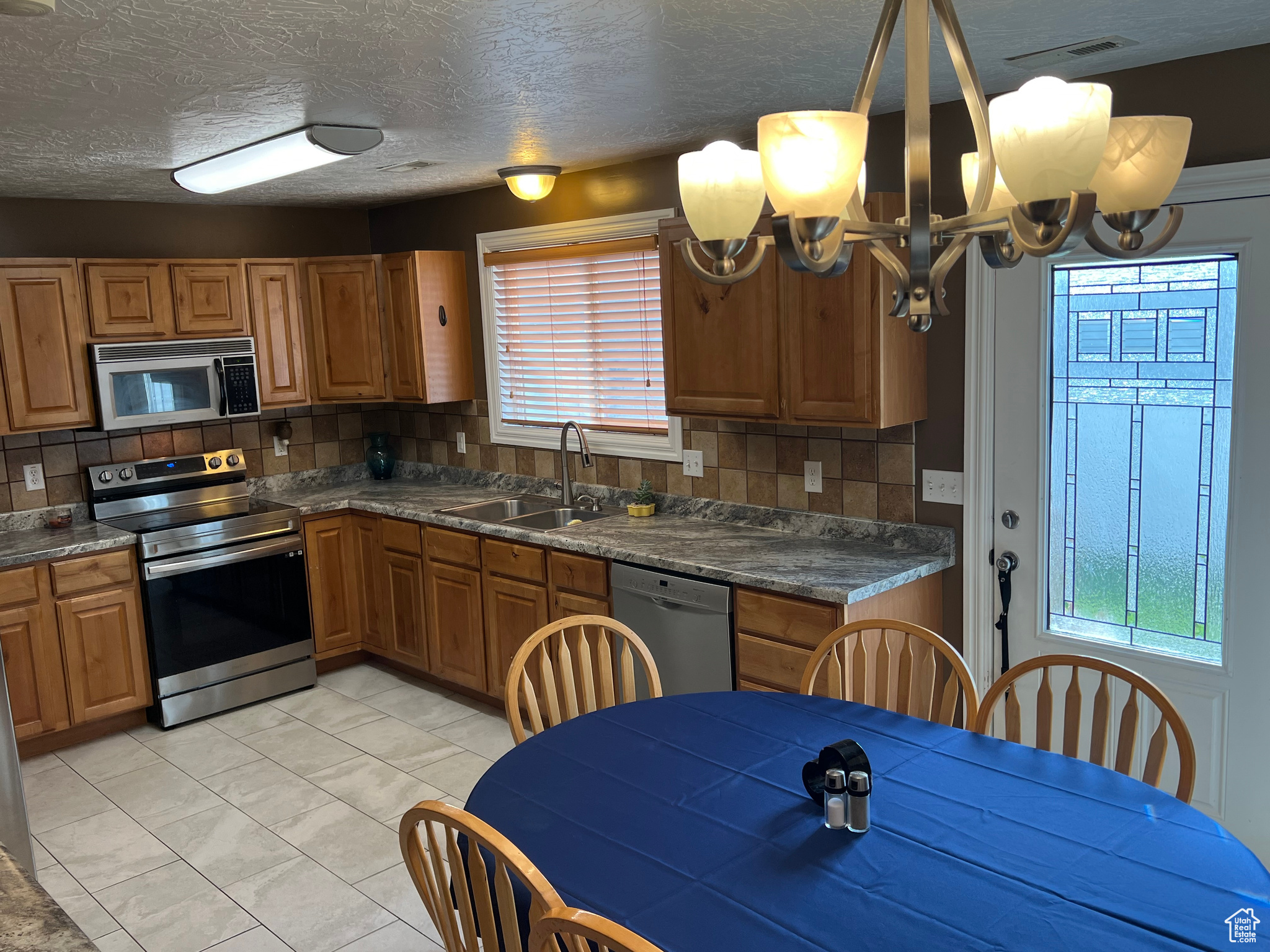 Kitchen featuring a notable chandelier, decorative backsplash, appliances with stainless steel finishes, and a healthy amount of sunlight