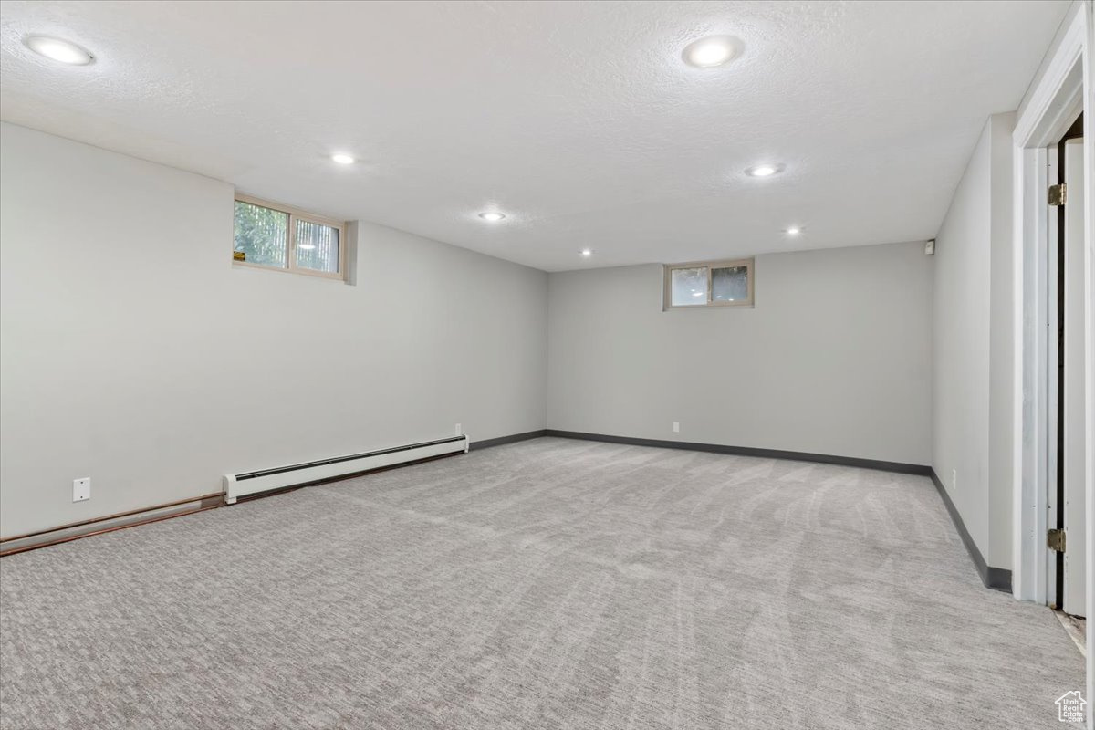 Carpeted empty room with a textured ceiling and a baseboard radiator