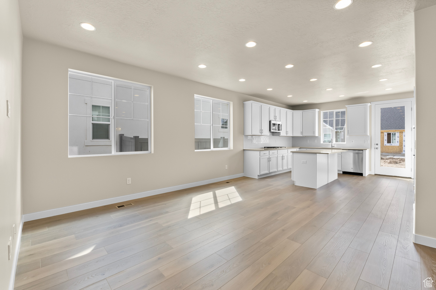 Kitchen featuring a kitchen island, a textured ceiling, light hardwood / wood-style flooring, white cabinetry, and appliances with stainless steel finishes