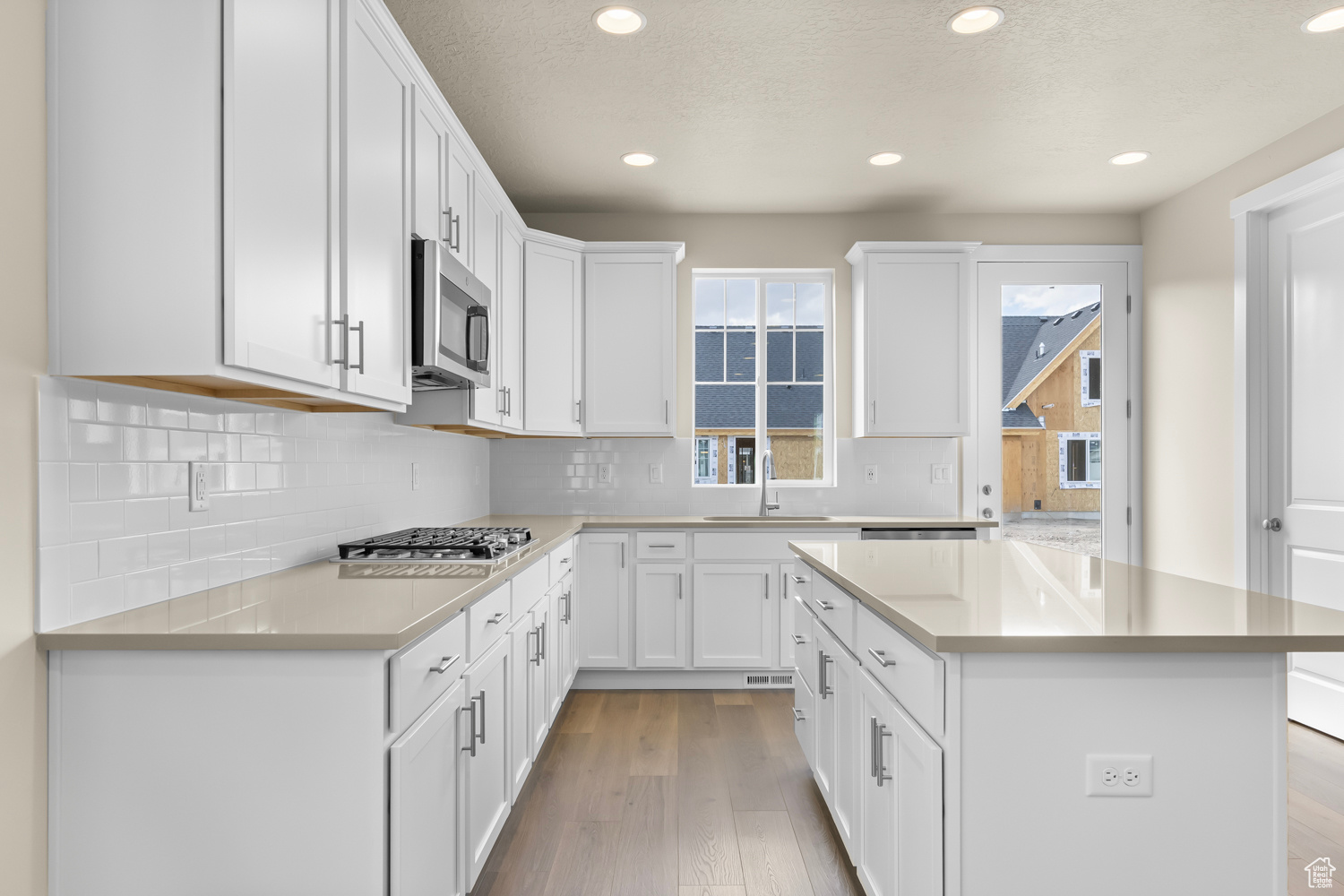 Kitchen with appliances with stainless steel finishes, white cabinets, a kitchen island, light wood-type flooring, and sink