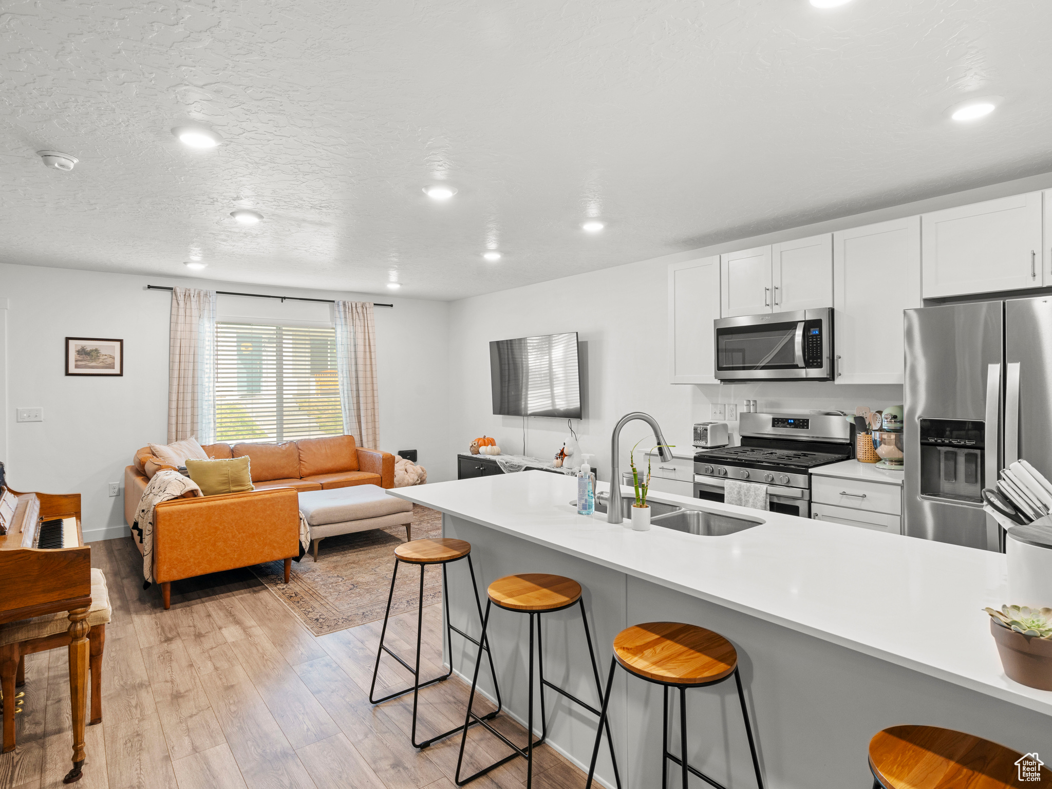 Kitchen with white cabinets, stainless steel appliances, a kitchen bar, light hardwood / wood-style flooring, and sink