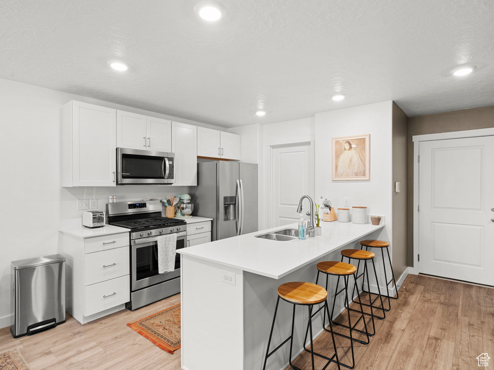 Kitchen with a breakfast bar, light wood-type flooring, sink, white cabinets, and stainless steel appliances