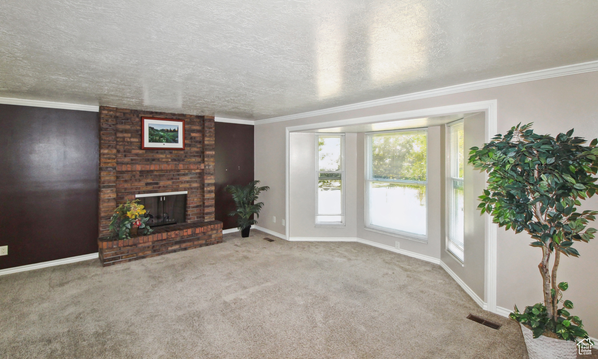 Spacious living room featuring a brick fireplace, bay window, and crown molding