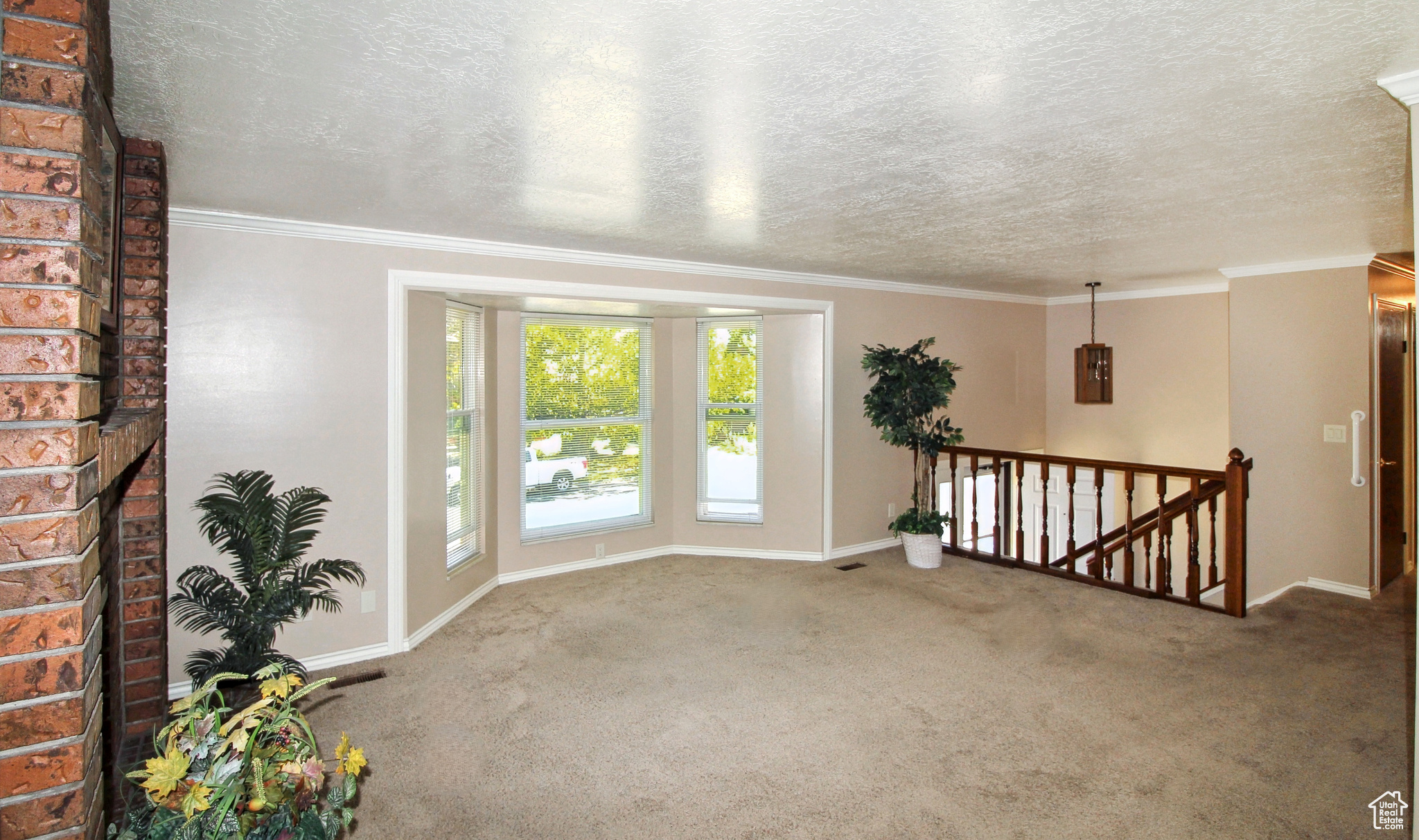 Spacious living room featuring a brick fireplace, bay window, and crown molding