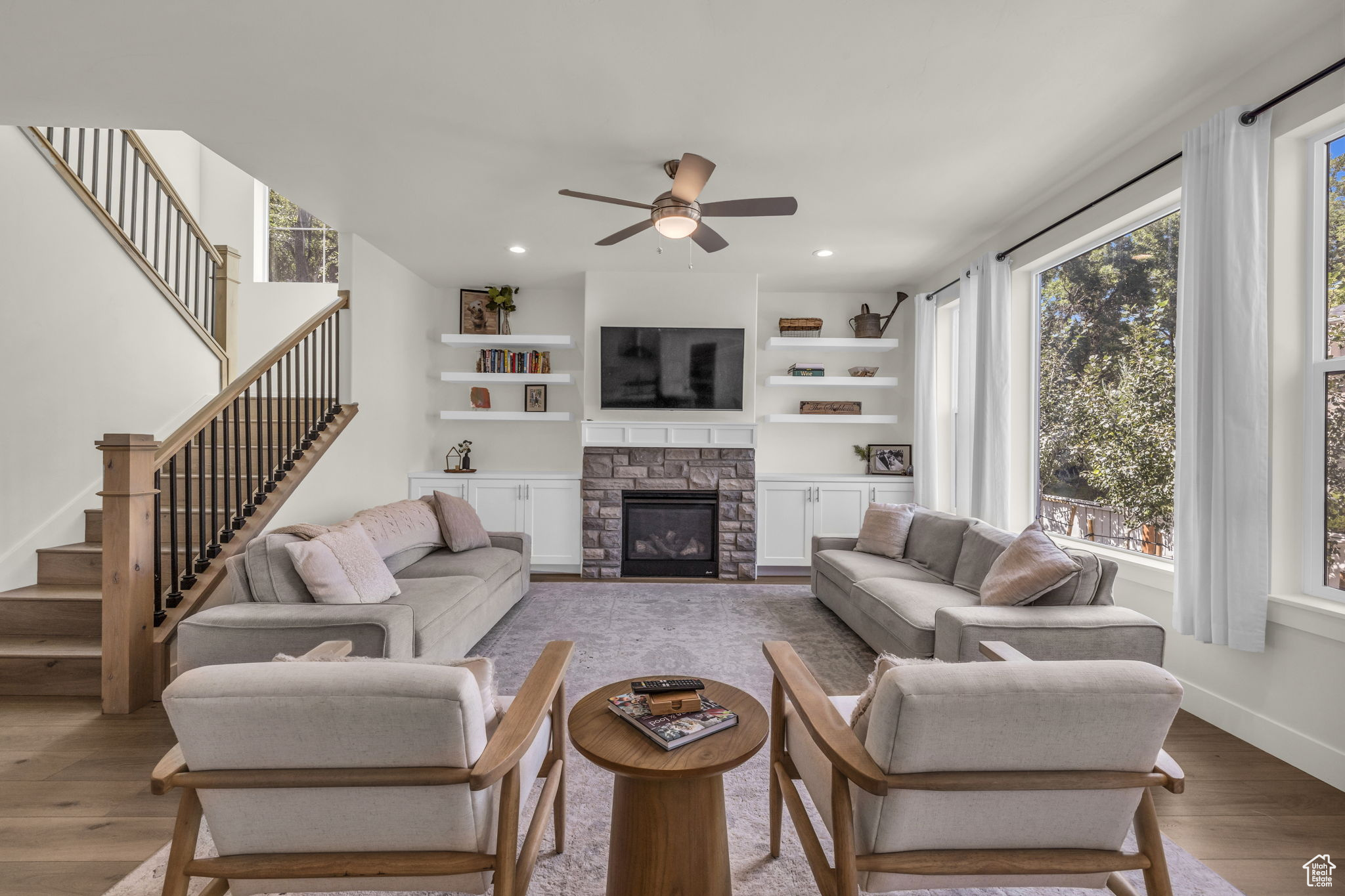 Living room featuring ceiling fan, a stone fireplace, plenty of natural light, and light hardwood / wood-style floors.