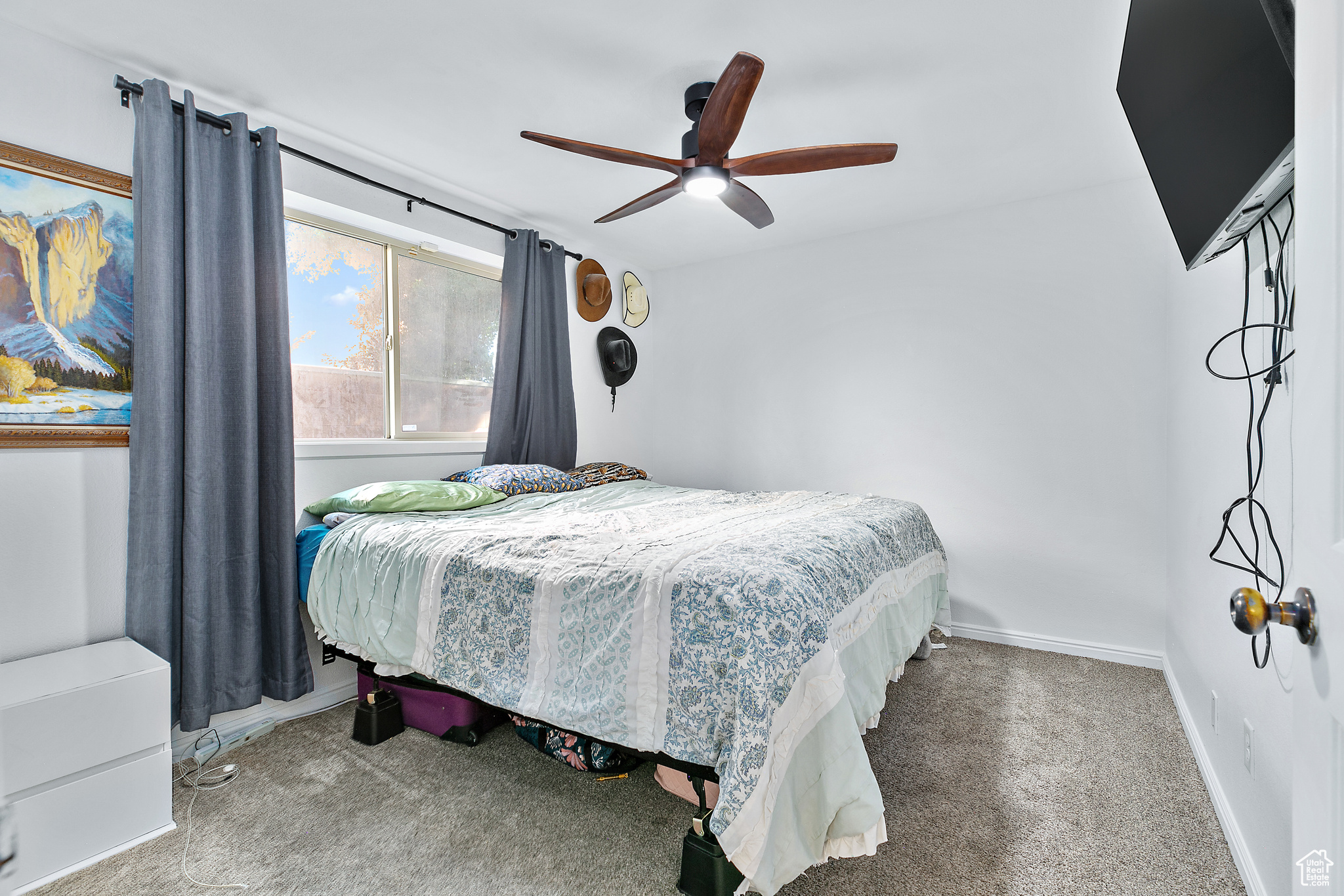 Carpeted bedroom featuring ceiling fan and drapery