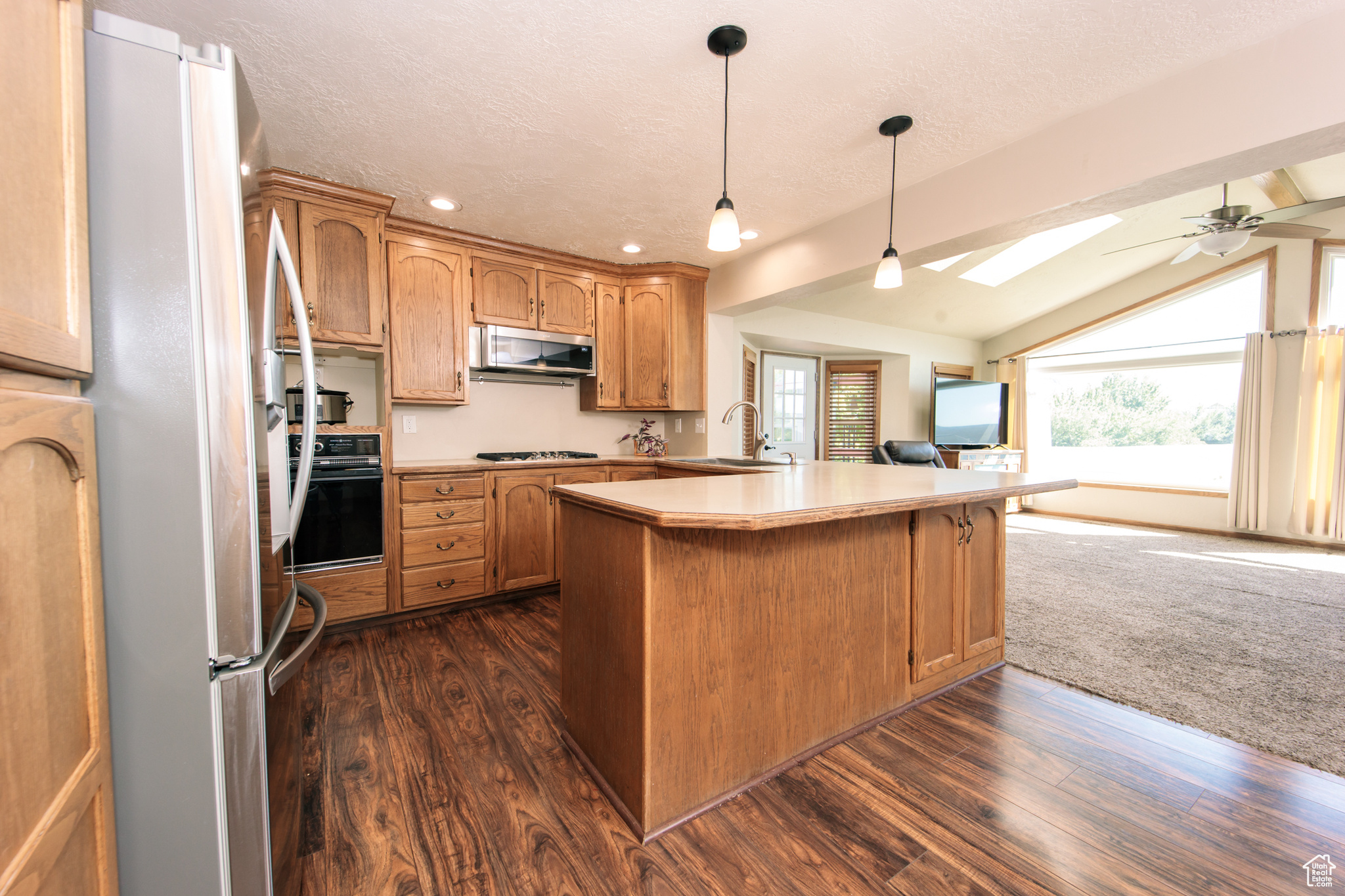 Kitchen with kitchen peninsula, black oven, lofted ceiling with skylight, refrigerator, and dark hardwood / wood-style floors