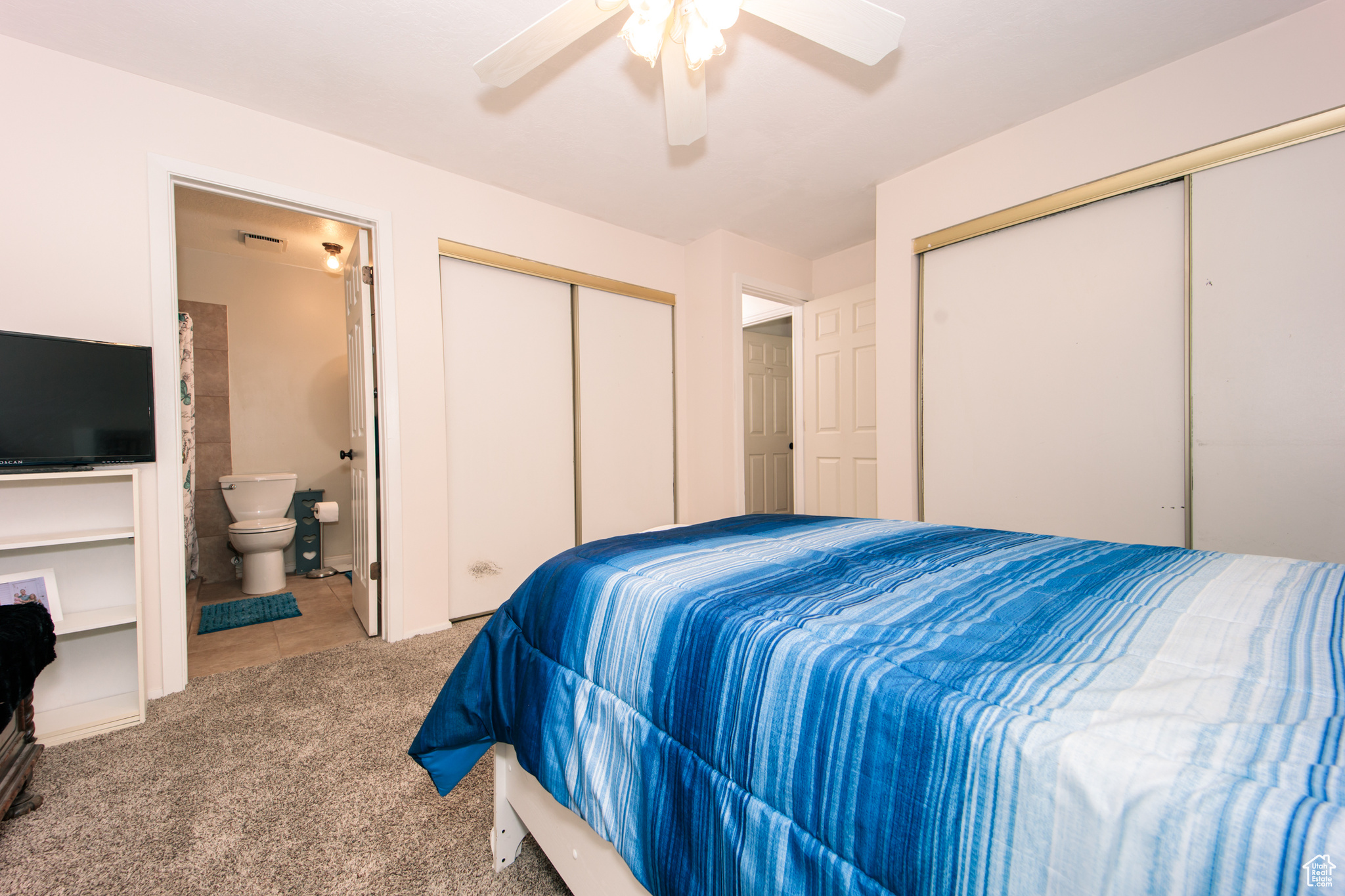 Carpeted bedroom featuring multiple closets, ceiling fan, and ensuite bathroom