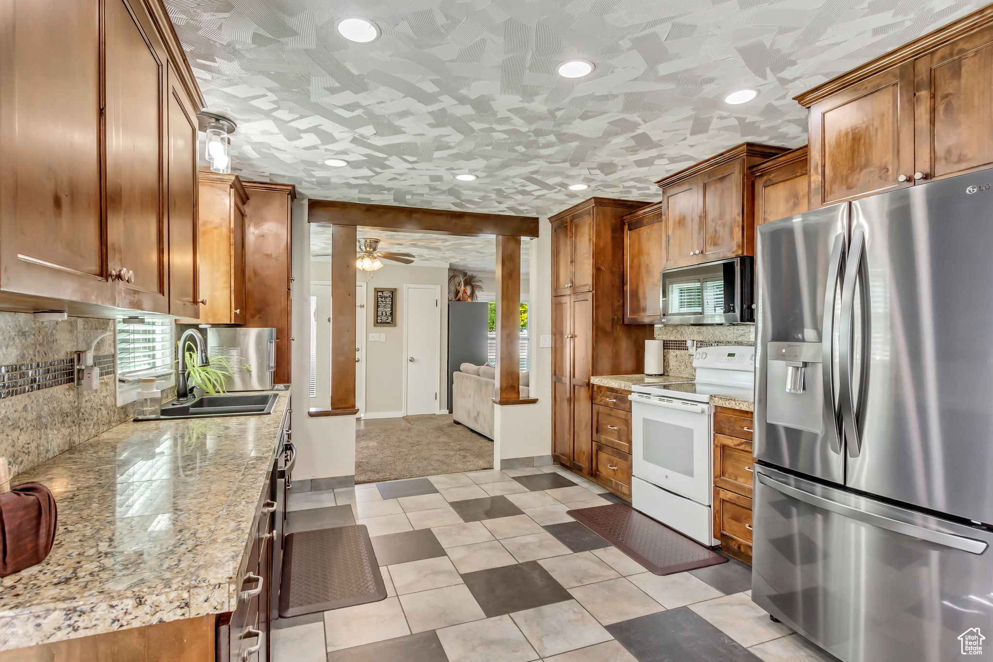 Kitchen with sink, backsplash, appliances with stainless steel finishes, light stone countertops, and ceiling fan