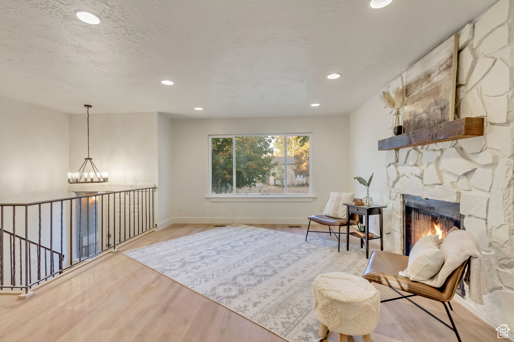 Sitting room featuring a stone fireplace, an inviting chandelier, light wood-type flooring, and a textured ceiling