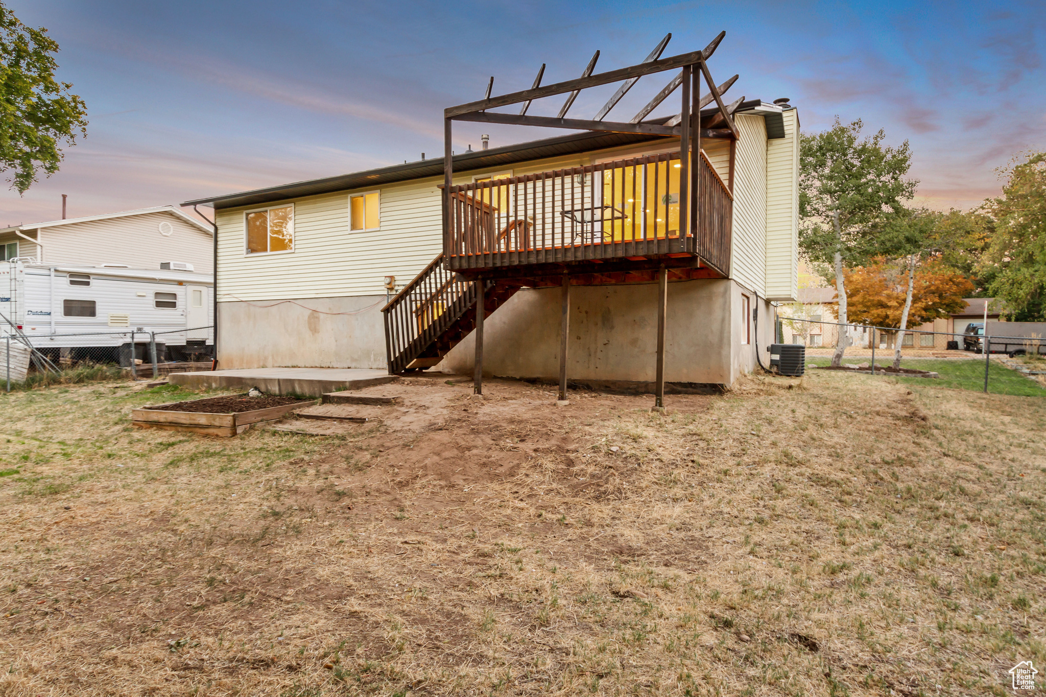 Back house at dusk with a lawn, central AC, and a deck