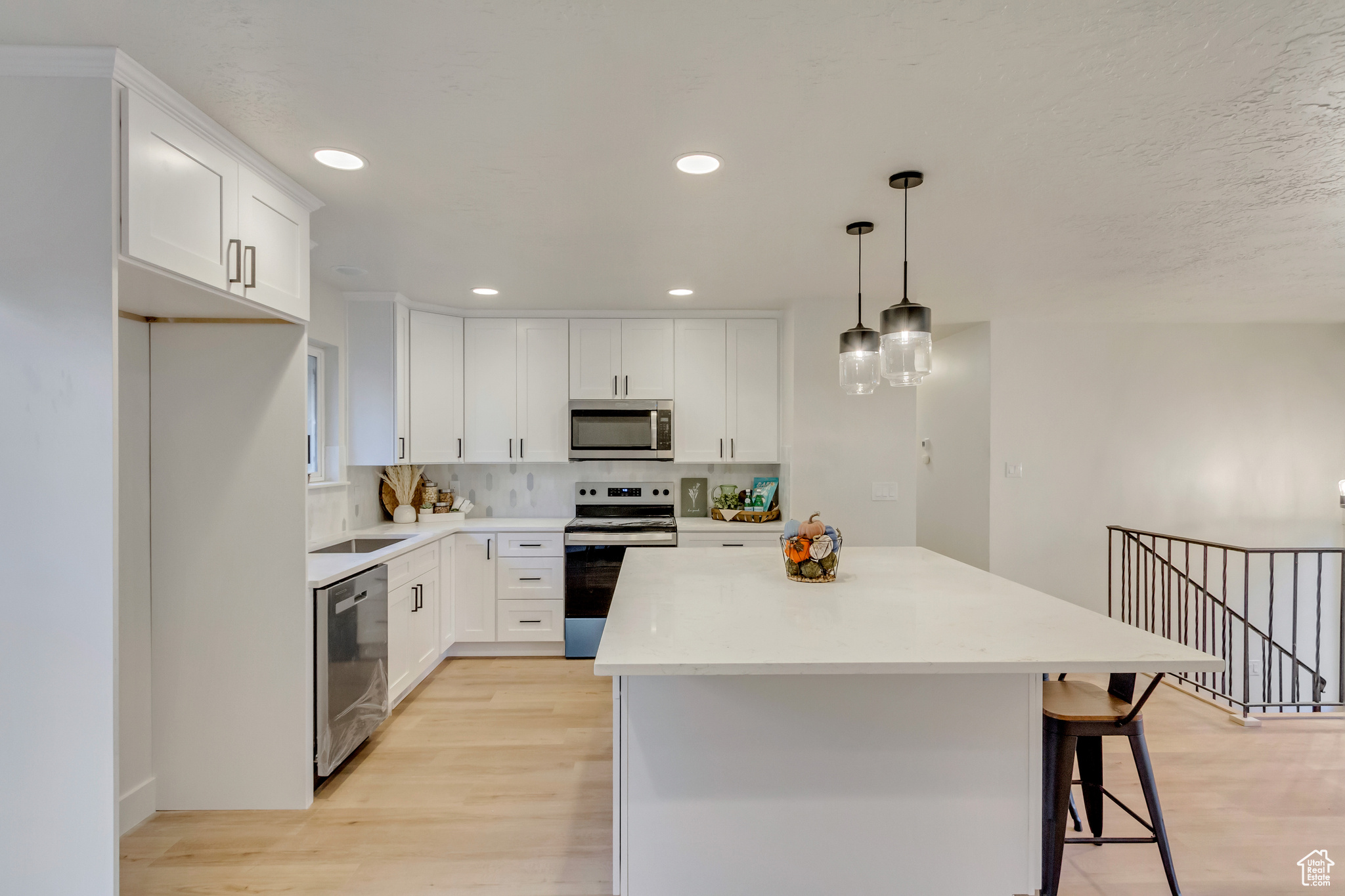 Kitchen with white cabinets, decorative light fixtures, stainless steel appliances, a center island, and light hardwood / wood-style floors