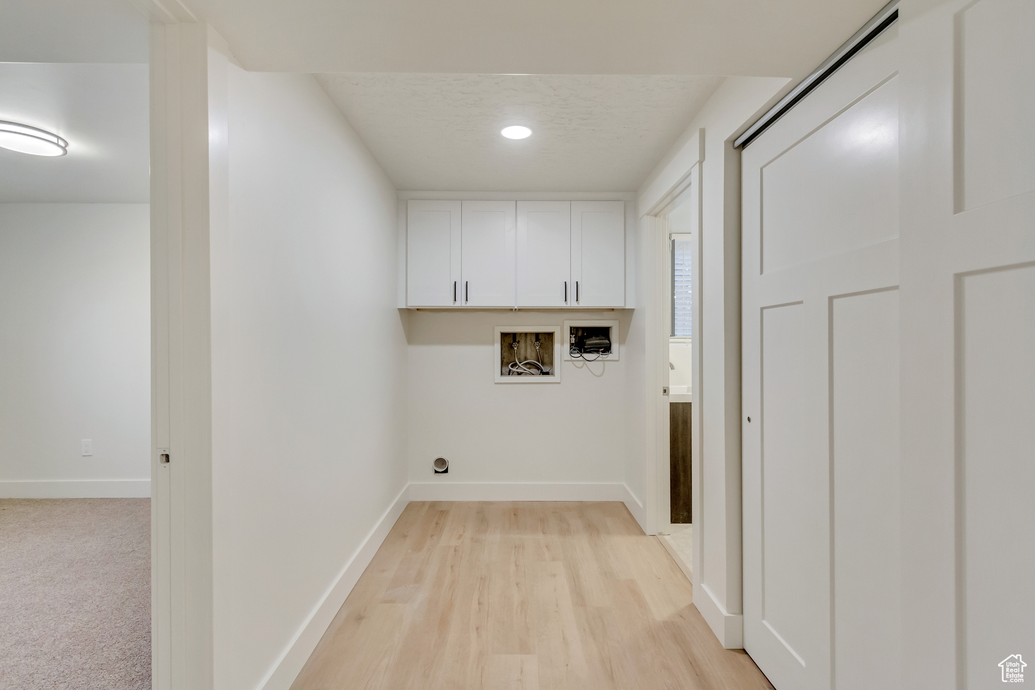 Clothes washing area featuring cabinets, light wood-type flooring, a textured ceiling, and washer hookup