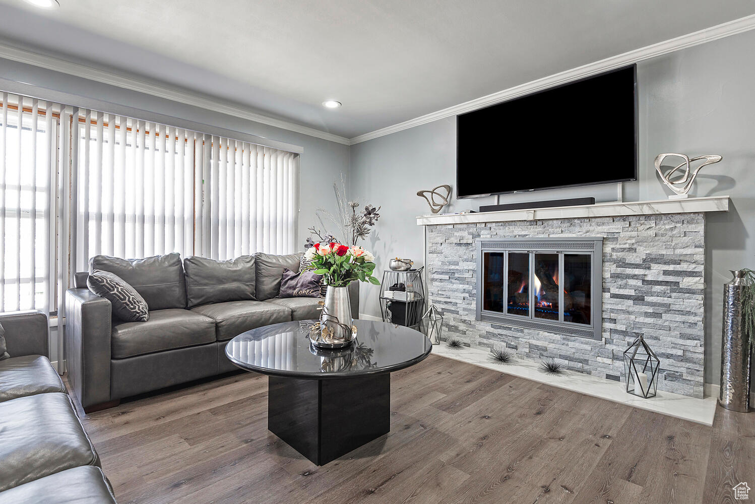 Living room featuring wood-type flooring, a stone fireplace, and crown molding