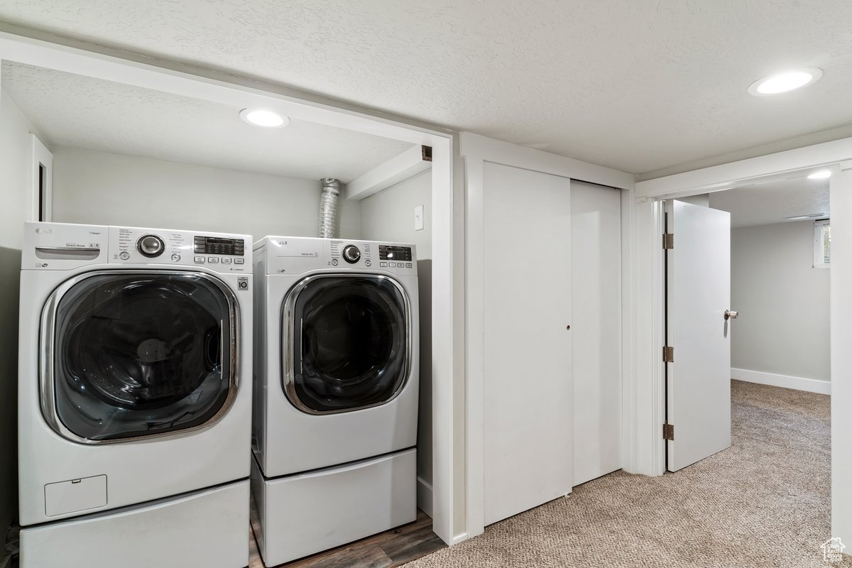 Clothes washing area with a textured ceiling, washing machine and dryer, and light colored carpet