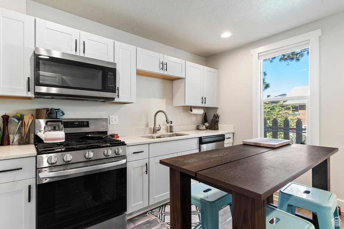 Kitchen with wood-type flooring, white cabinets, stainless steel appliances, and sink