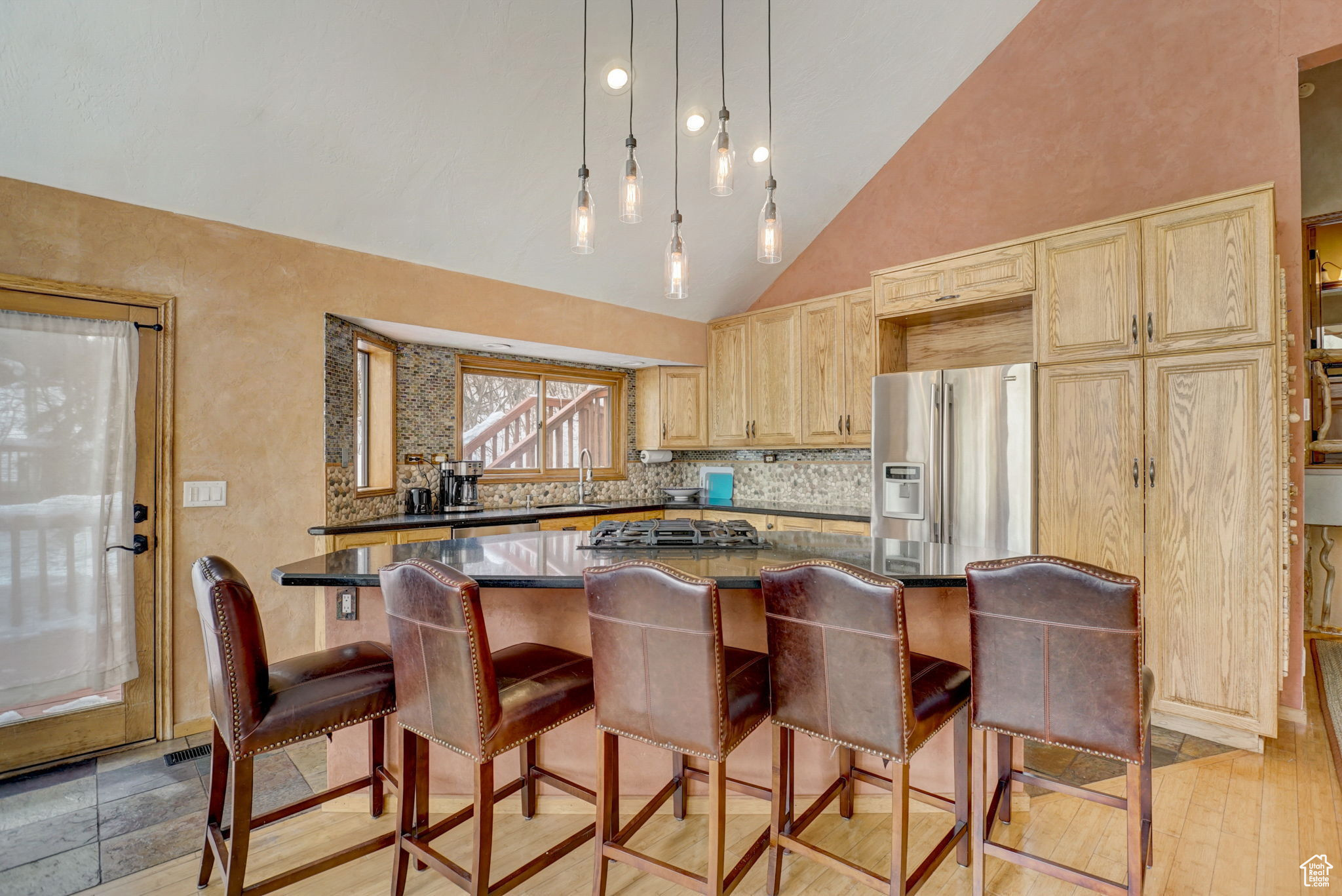 Kitchen featuring stainless steel fridge, high vaulted ceiling, light brown cabinets, decorative light fixtures, and sink